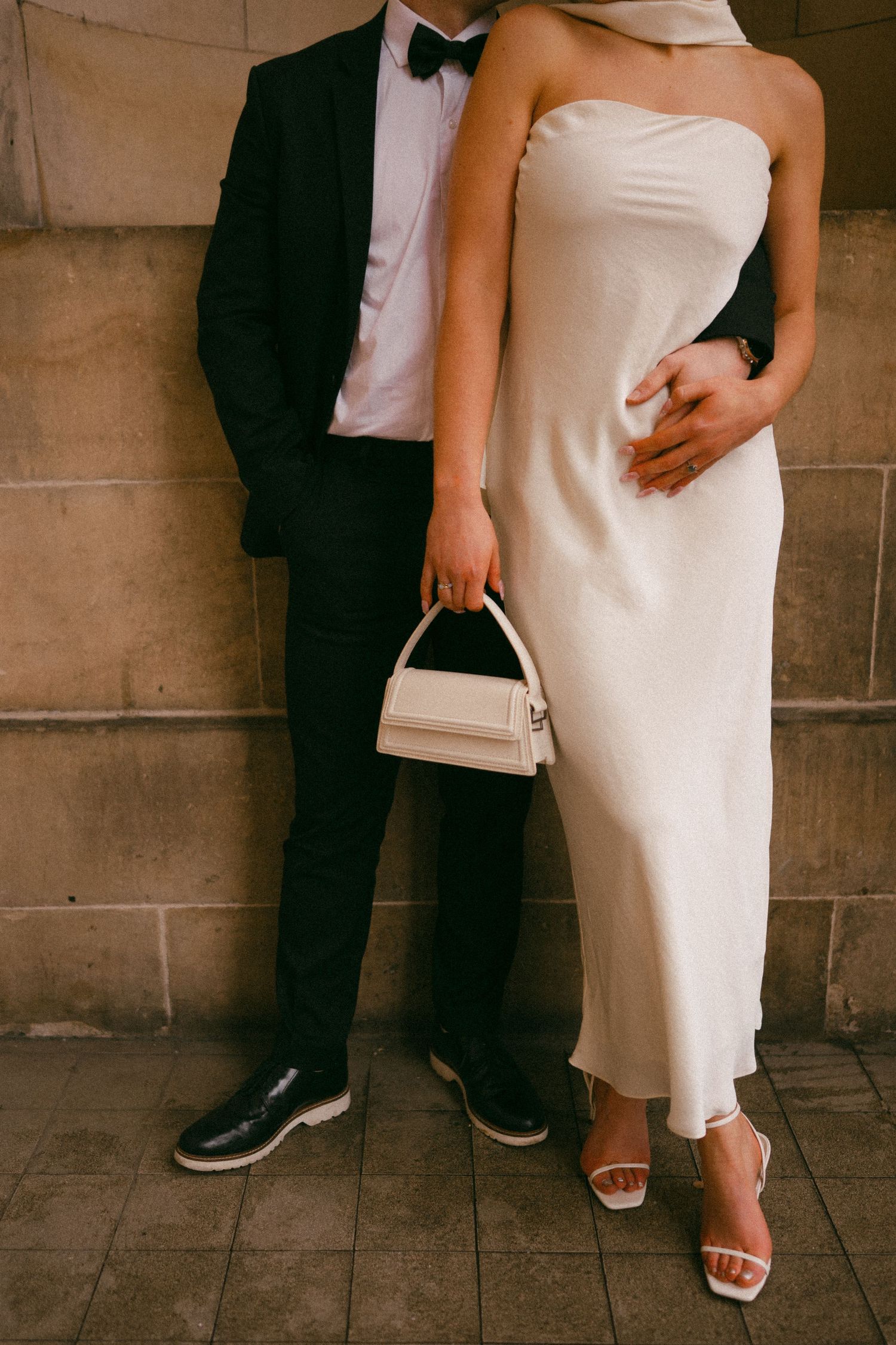 Cropped formal wedding photo showing elegant white dress and black tuxedo details against stone wall. Edinburgh Elopement