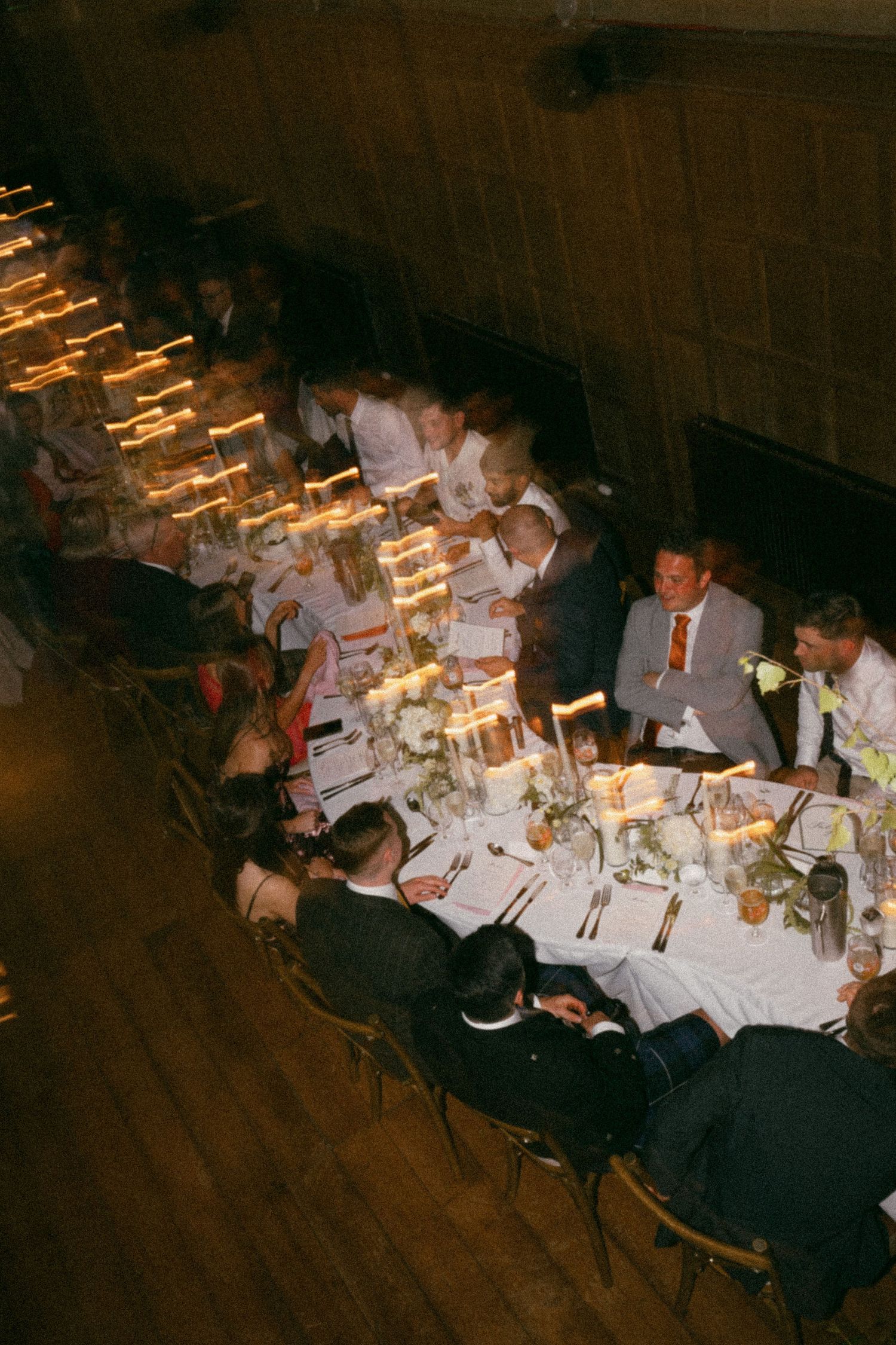 Guests seated at a long dimly lit dinner table with glowing candles creating an intimate ambiance at a formal event.