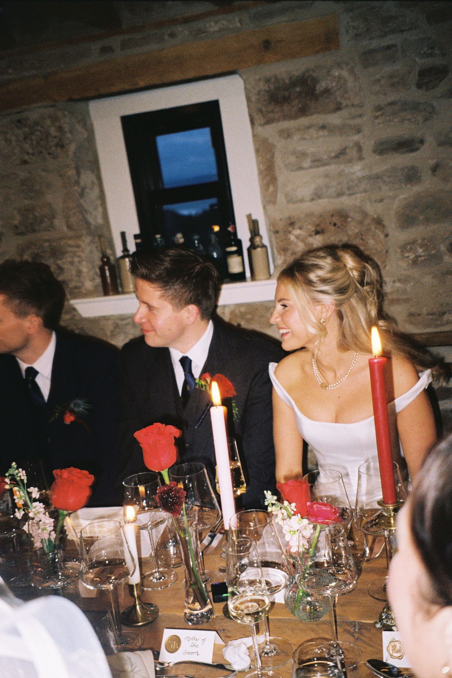 Guests seated at an elegant candlelit dinner table in a rustic stone-walled room during a formal event.