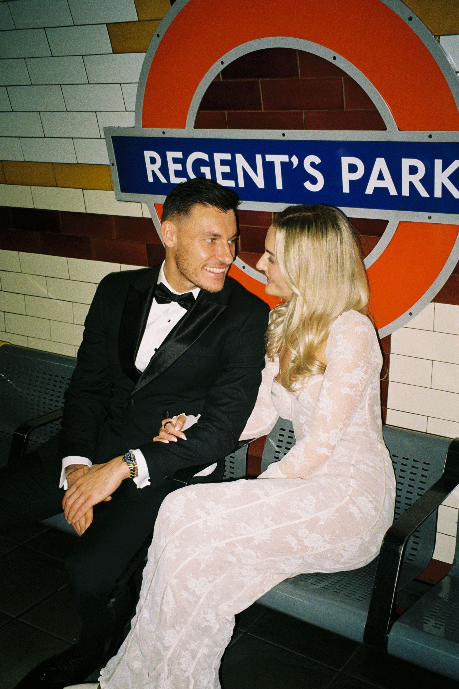 A couple in formal attire sit together on a bench at Regent's Park tube station in London.
