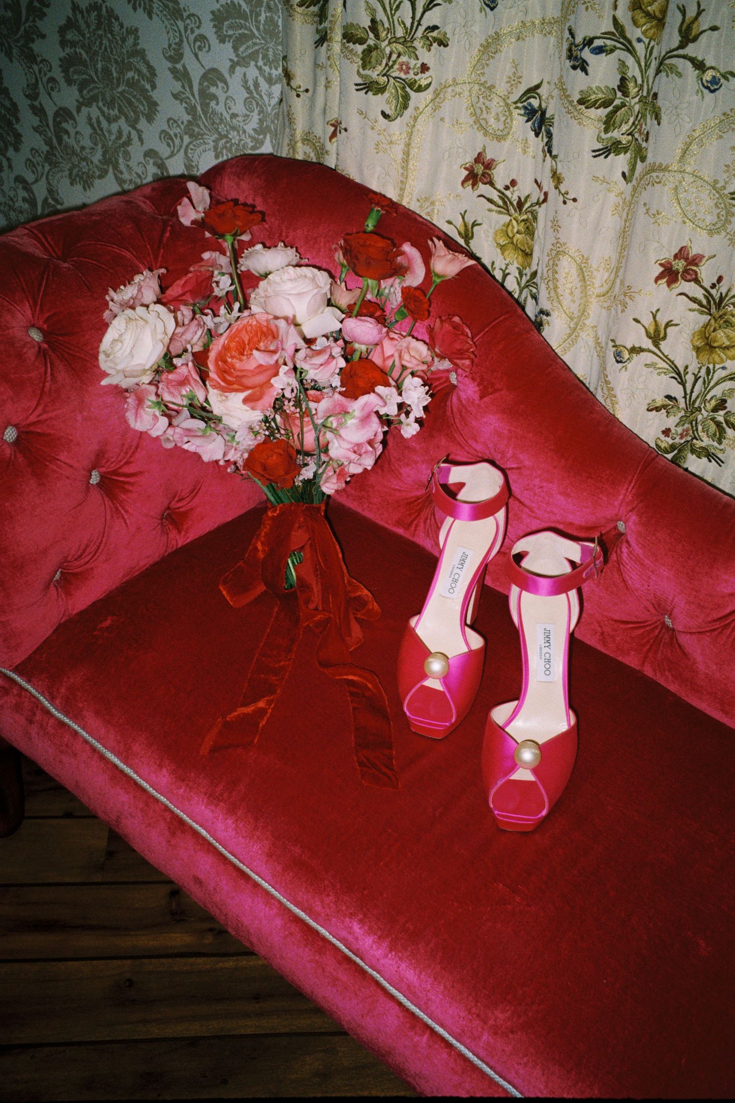 Pink and white flowers arranged in a vase on a plush red velvet couch or bench surface.