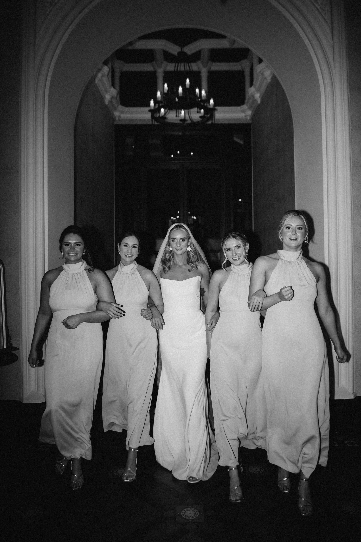 Wedding party wearing matching white gowns walk together.  Aberdeen wedding photographer, kinnettles castle, direct flash, bridal party