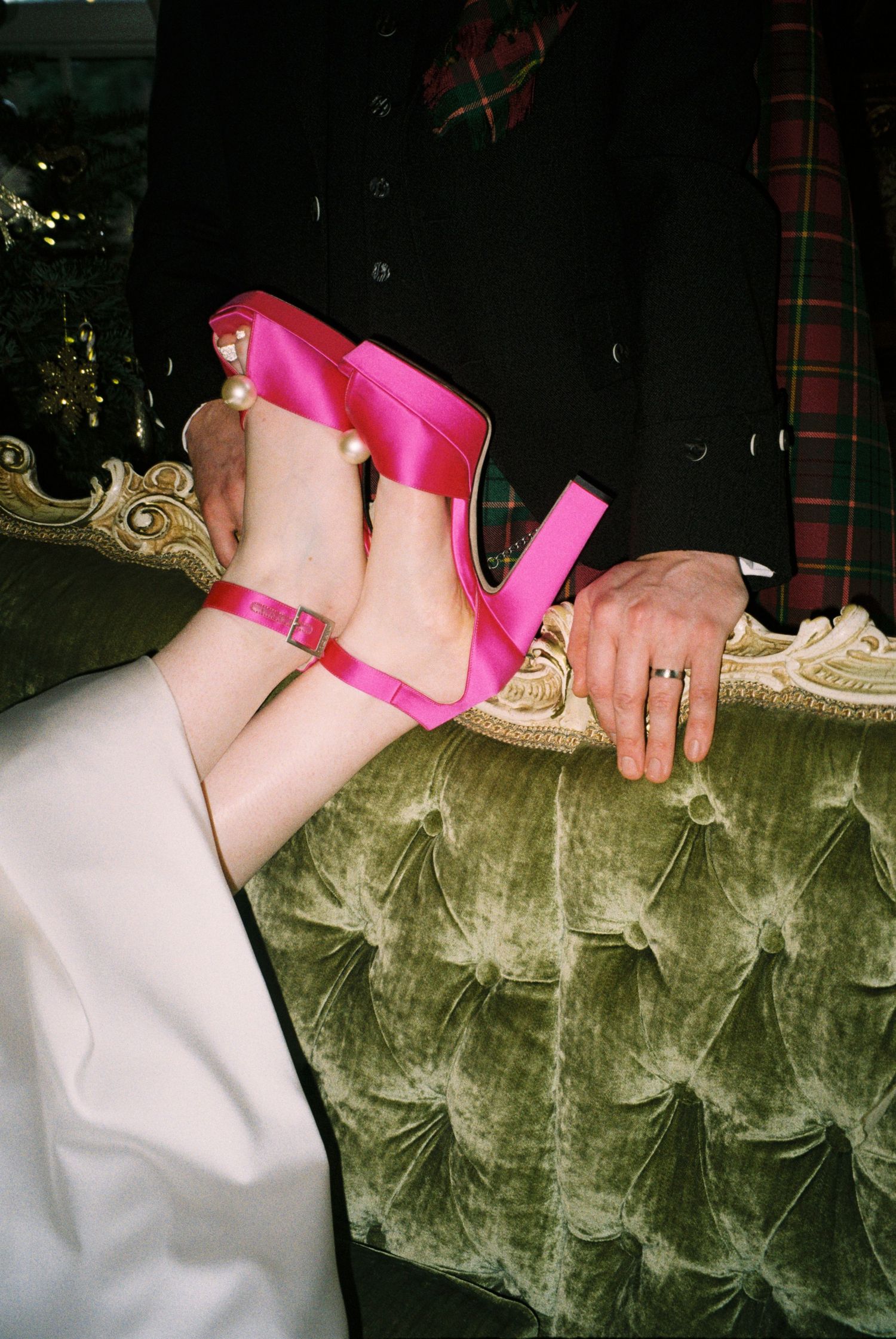 Pink bondage restraints secured to an olive green velvet couch in a dark room with plaid decor.