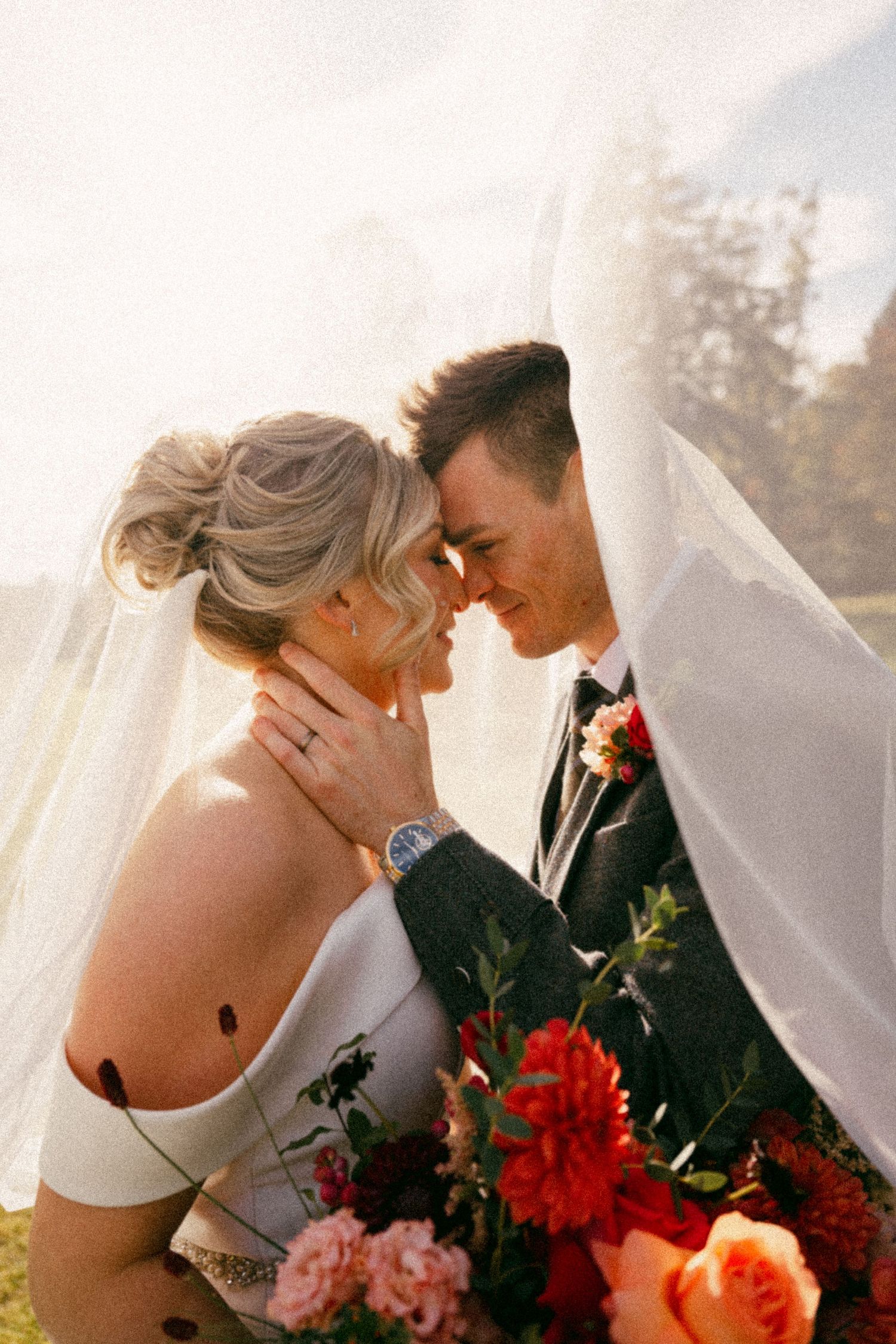 A romantic wedding couple shares a tender moment under a veil with coral and red flowers. Aberdeen wedding photographer, raemoir house weddi