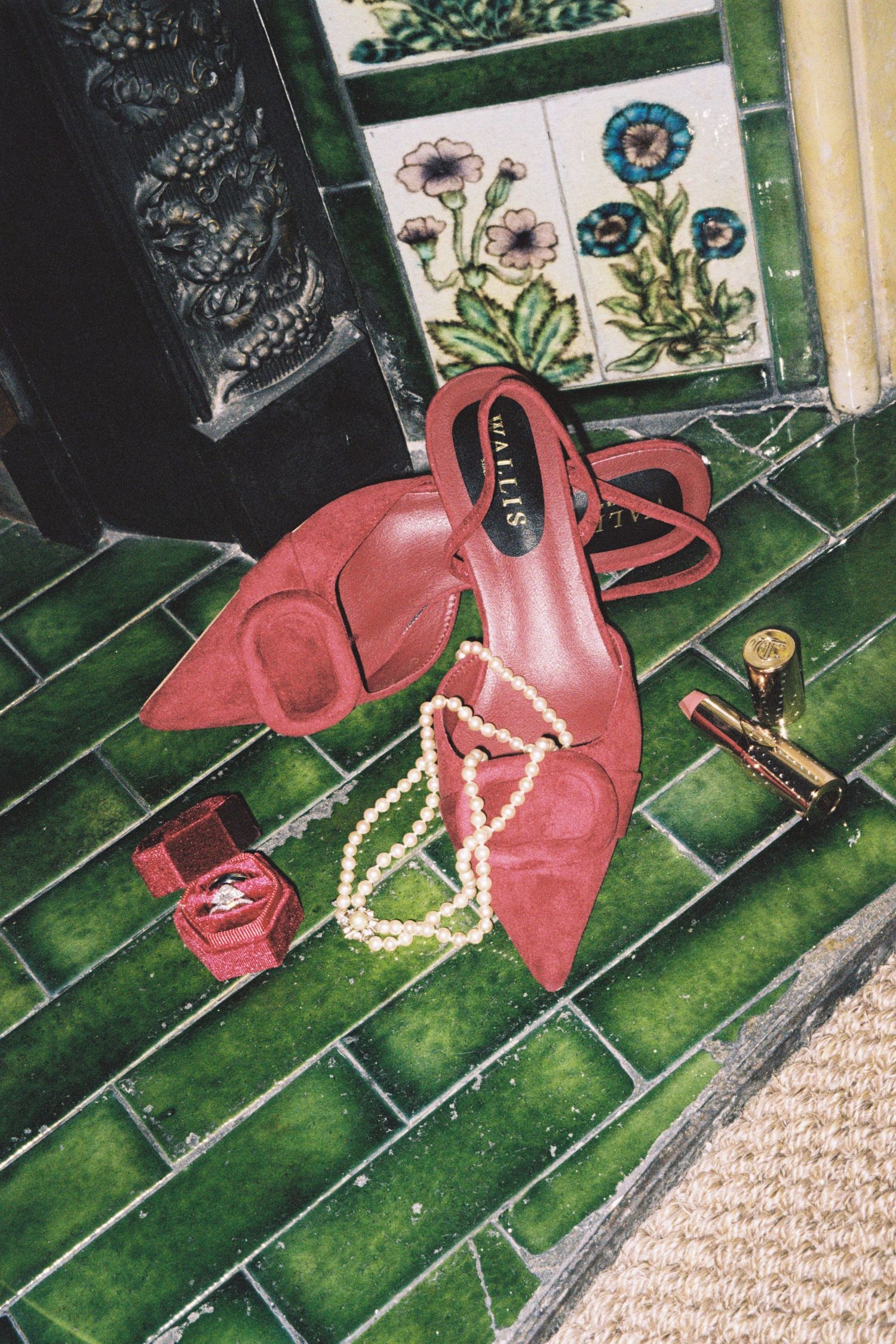 A sequence of red high heel shoes arranged on green carpeted stairs with a pearl necklace draped across them.