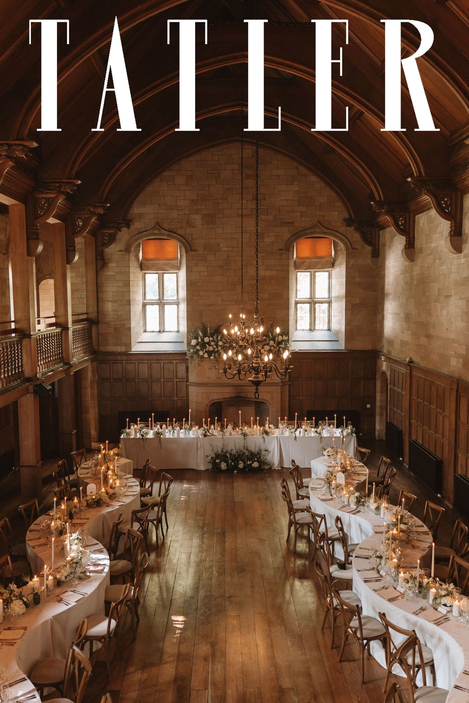 Long rustic banquet tables set for an elegant wedding reception in a historic wooden beam hall with warm lighting.