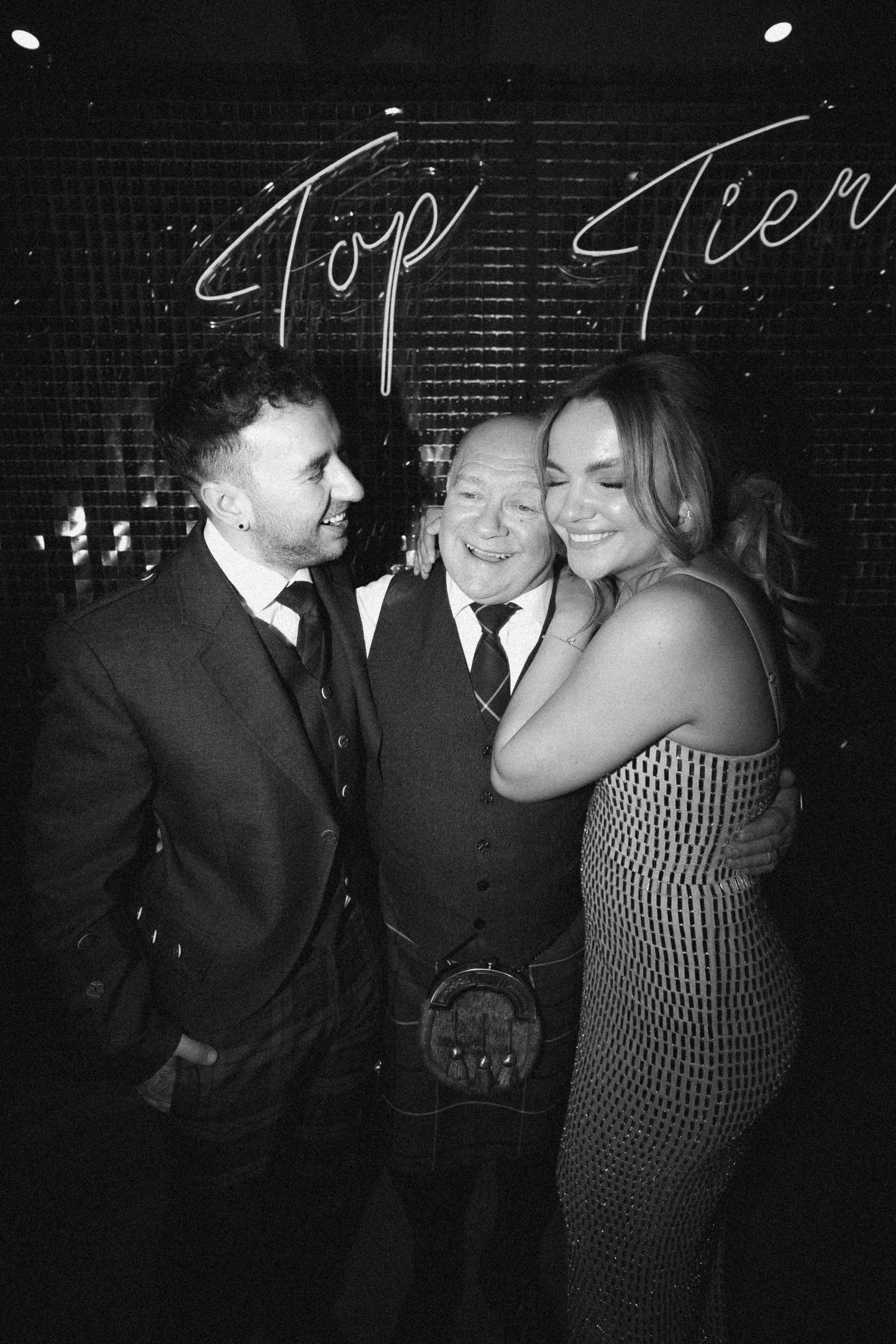 Celebratory moment captured under neon 'Top Tier' sign at an evening event.  Aberdeen wedding photographer. top tier winner
