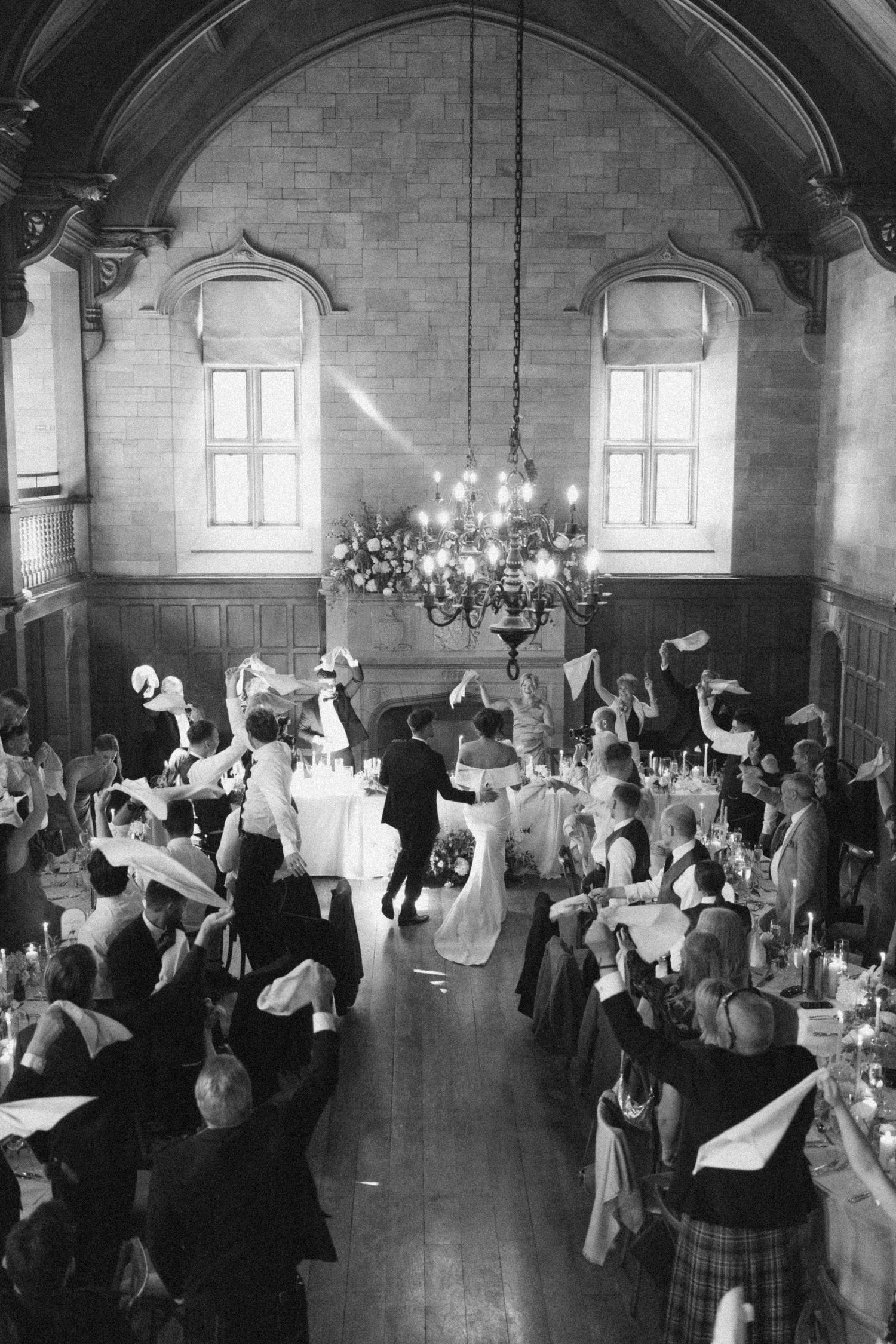 A vintage black and white photograph shows guests dancing at an elegant wedding reception in a grand vaulted hall.