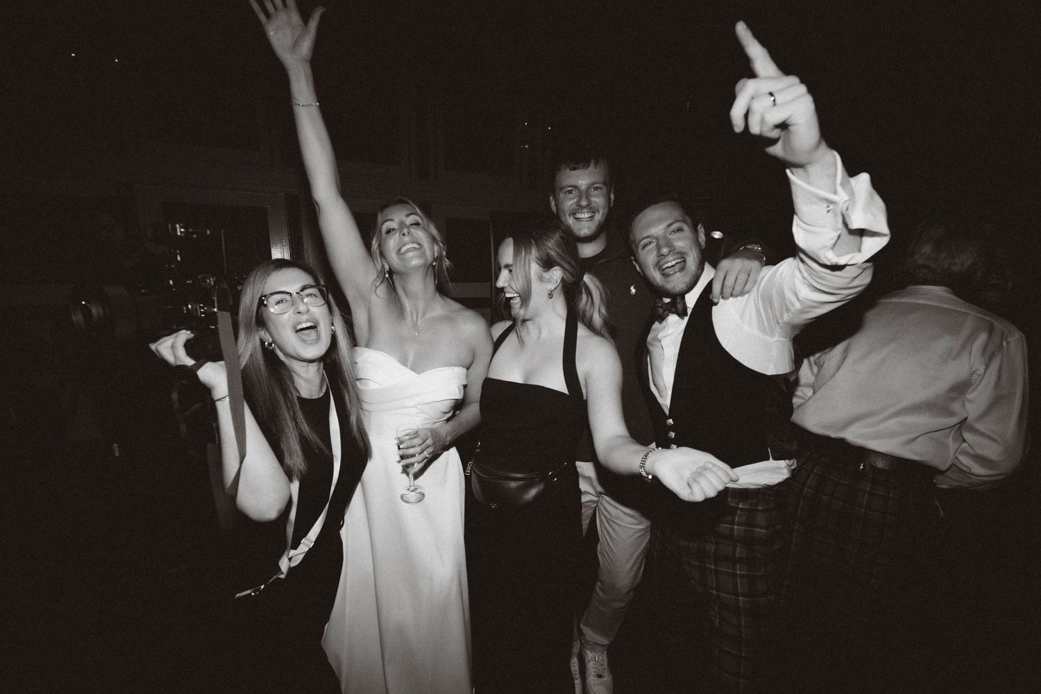 People dancing and having fun at a nightclub with dark lighting and raised hands in the air.