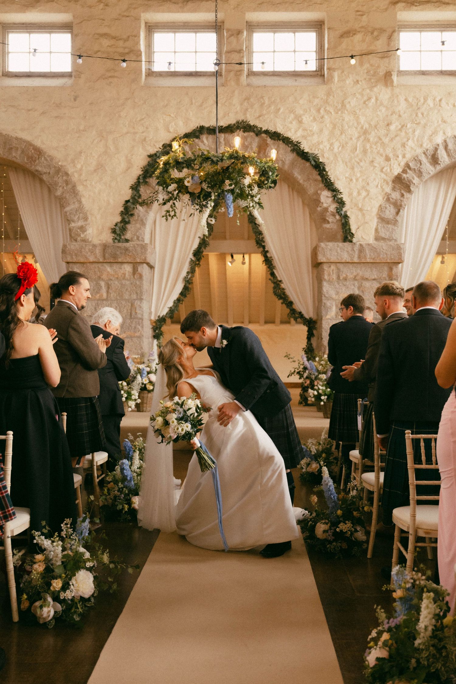 A wedding ceremony sequence showing guests seated in an elegant stone venue with floral arches and white drapes.