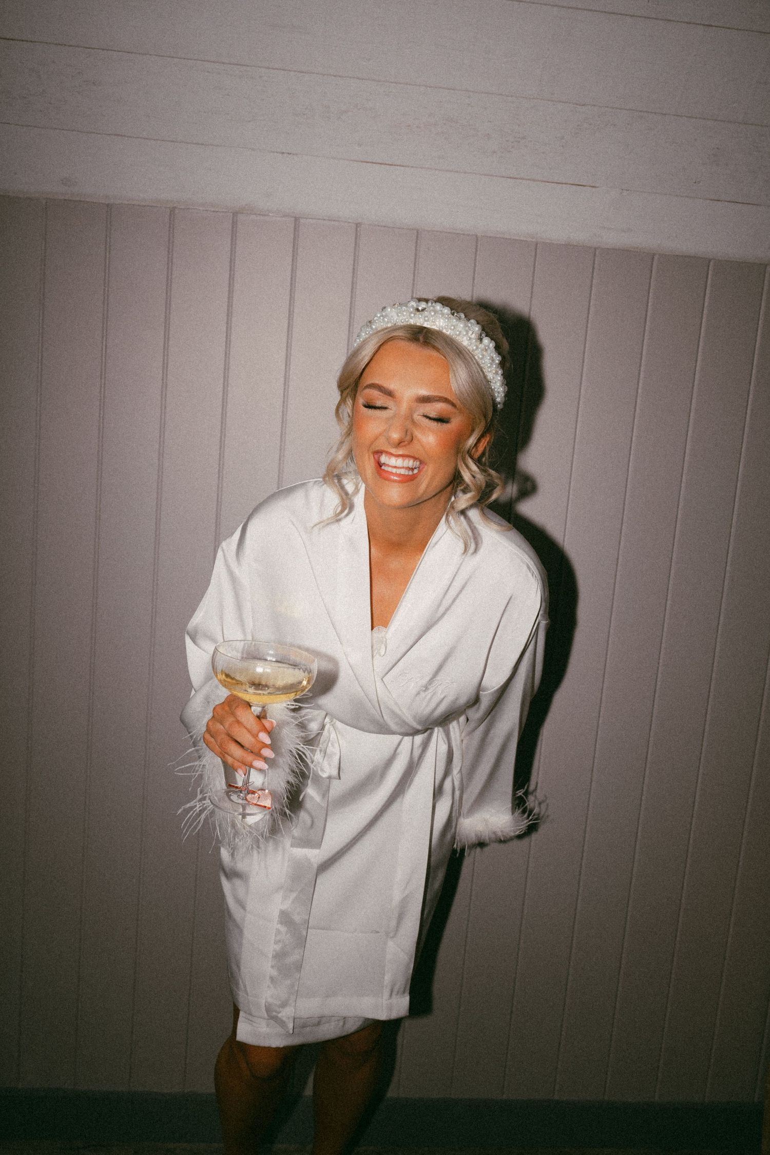 Joyful bride in white robe holding champagne glass during wedding preparations. Aberdeen wedding photographer, Barra barn, direct flash