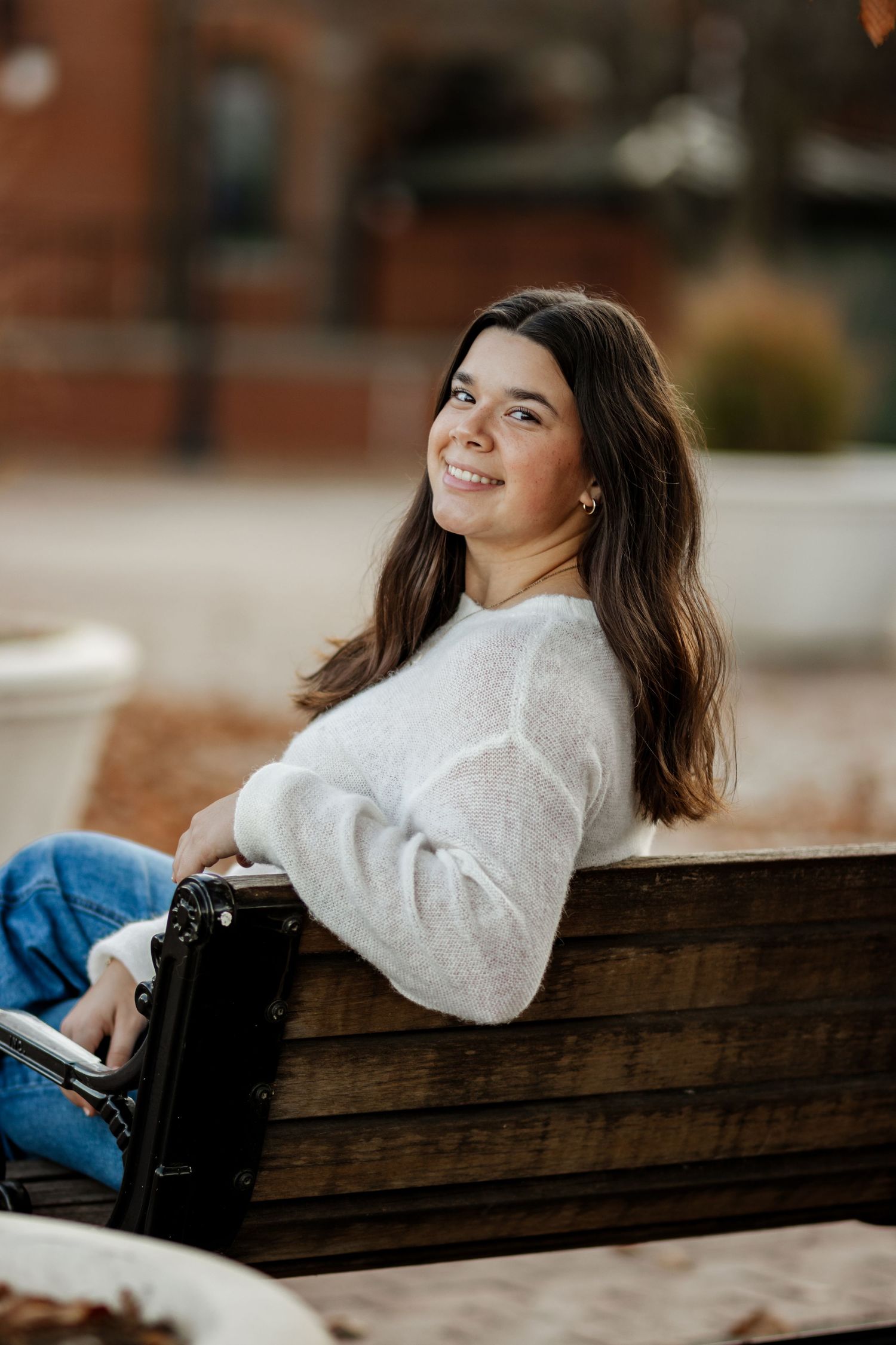 A person in a white sweater and jeans reclines on a rustic wooden bench in an outdoor setting.