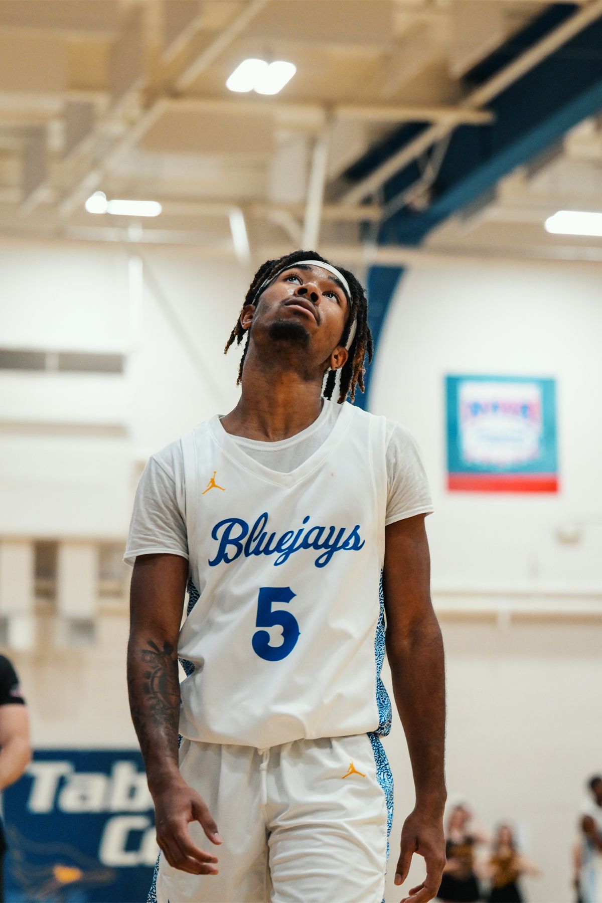 Basketball player in white Bluejays jersey number 5 looks upward during indoor game.