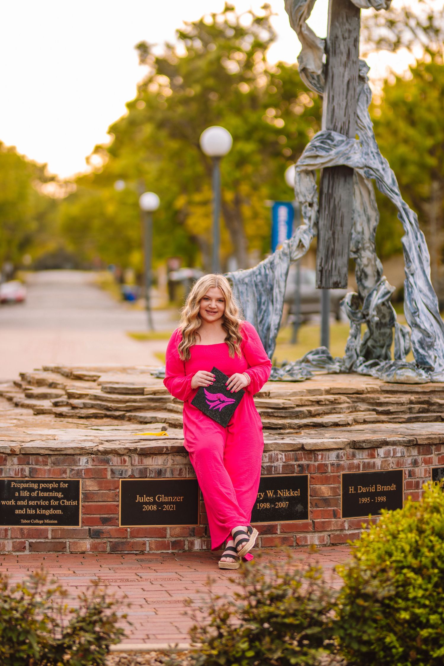 Person in bright pink outfit poses on memorial brick wall at sunset.