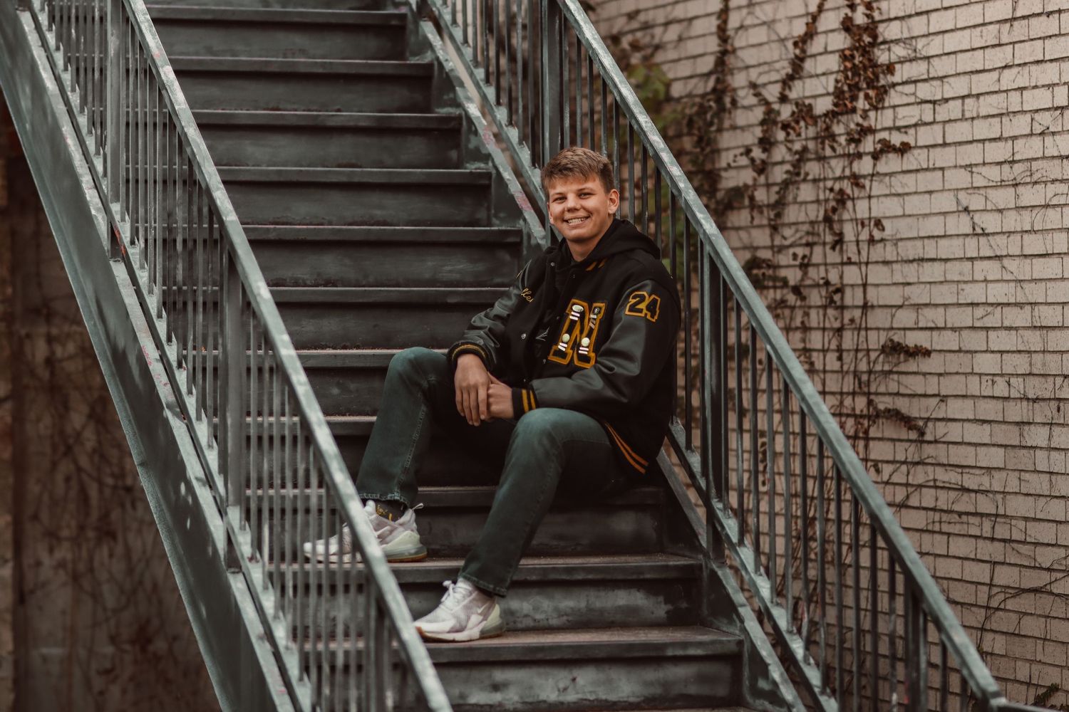 Person in dark clothing sitting on metal stairs against brick wall.