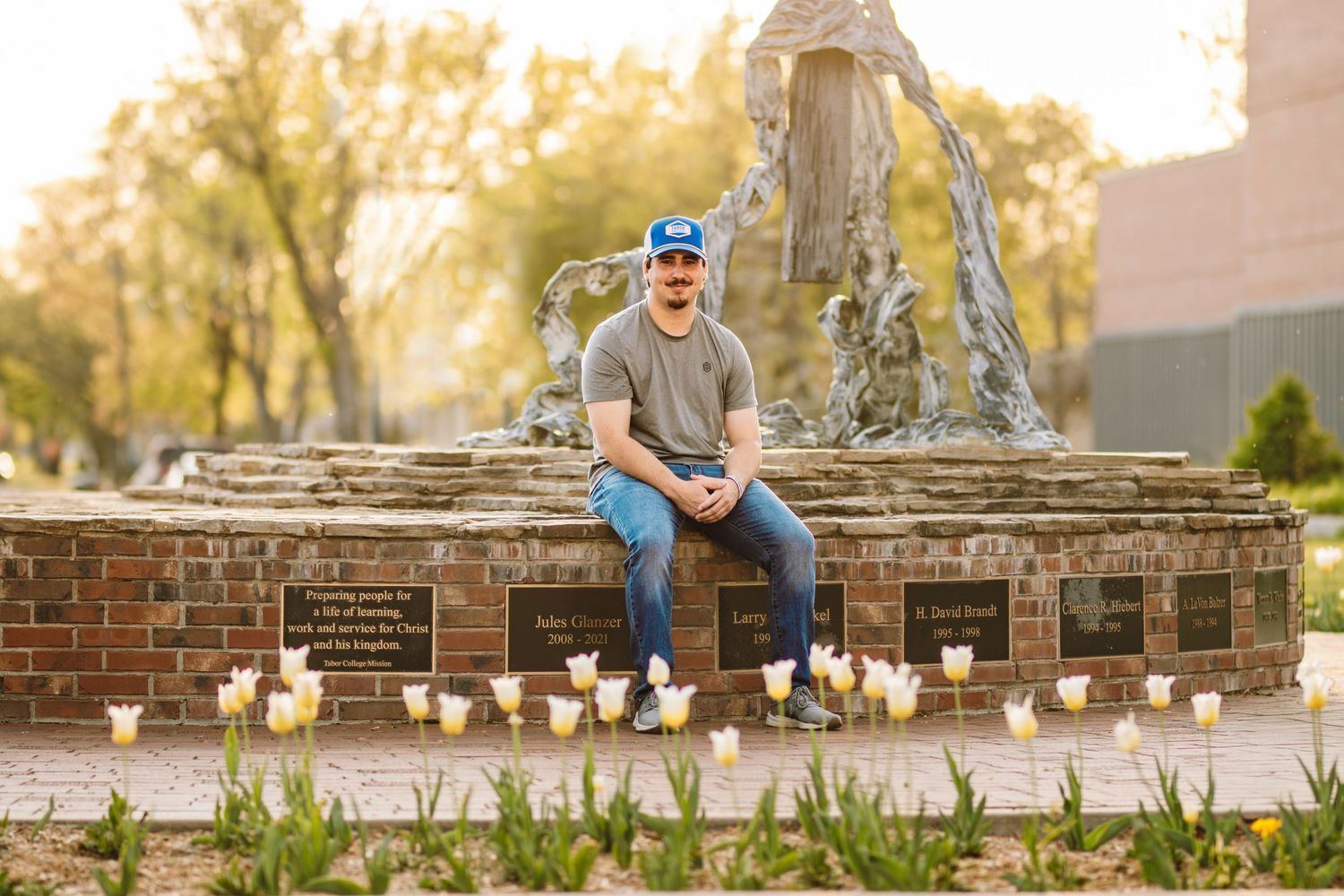 A photographer poses with toy rubber ducks lined up on a brick wall at sunset.