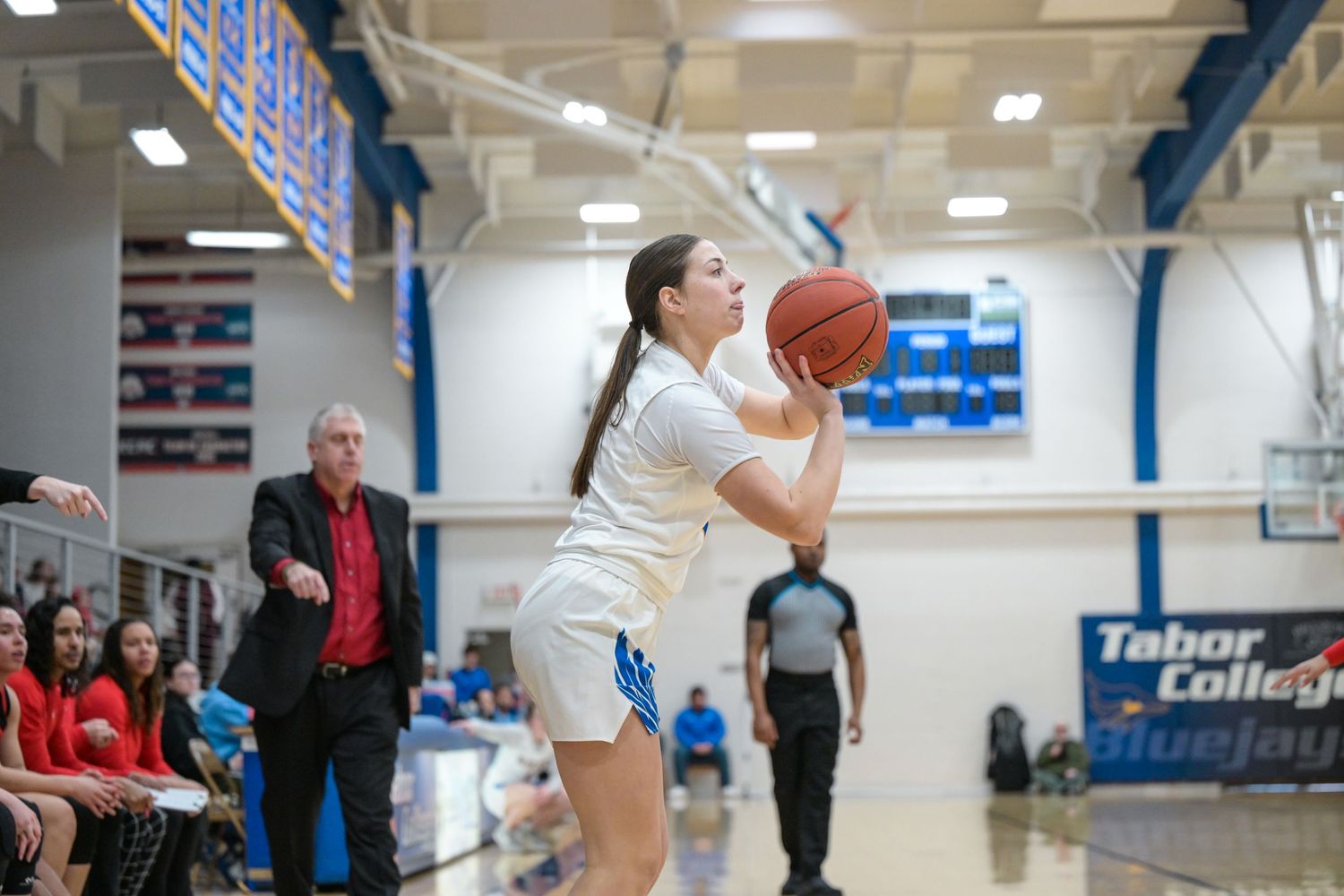 Player takes aim for a shot during basketball game in college gymnasium.