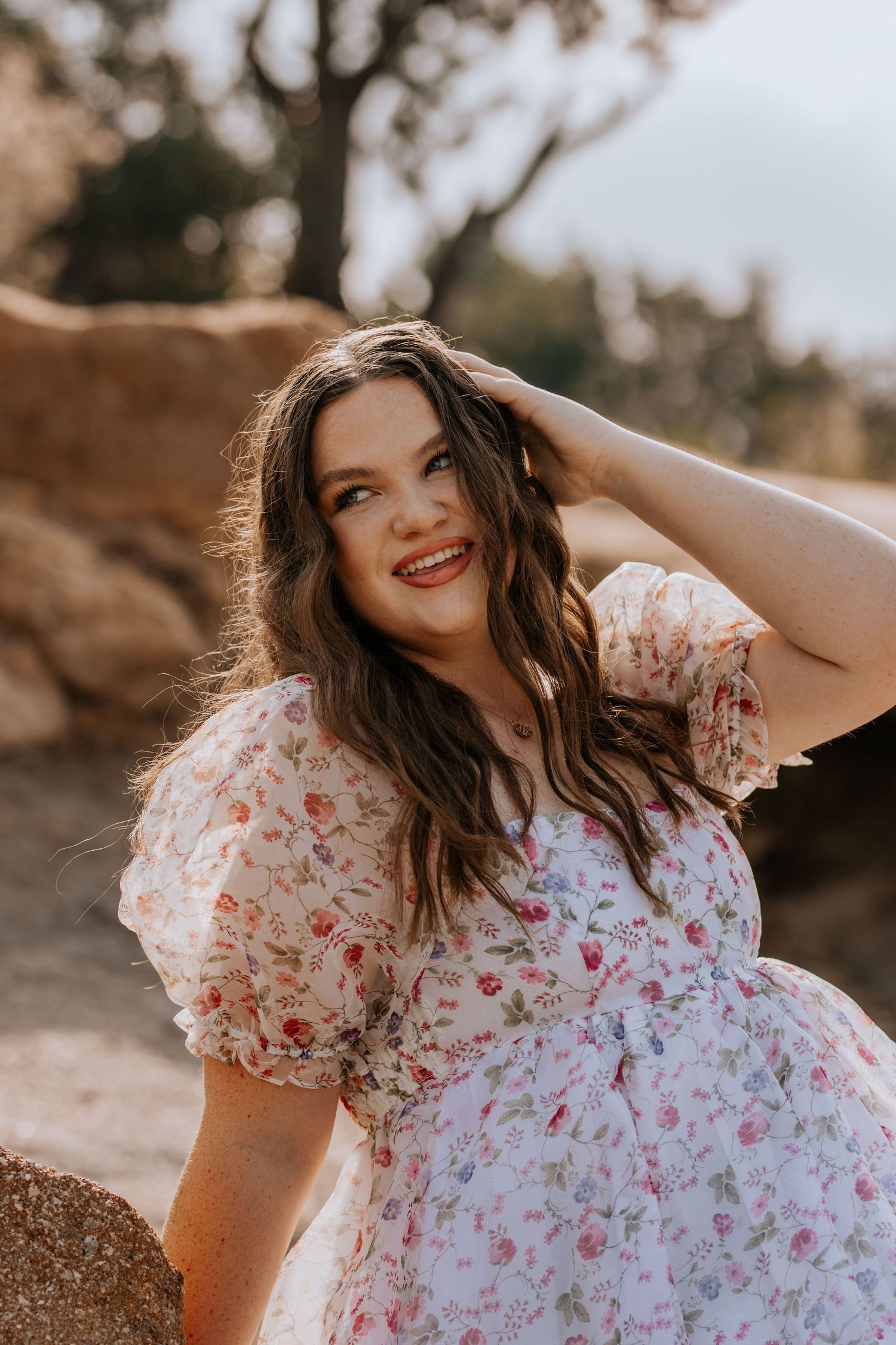 A woman in a white floral dress poses outdoors in warm sunlight creating a dreamy summer portrait series.