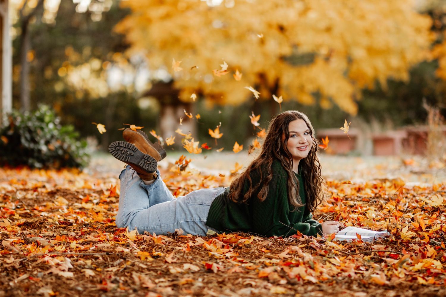 A couple lies together on fallen autumn leaves during a romantic fall photoshoot in a park.