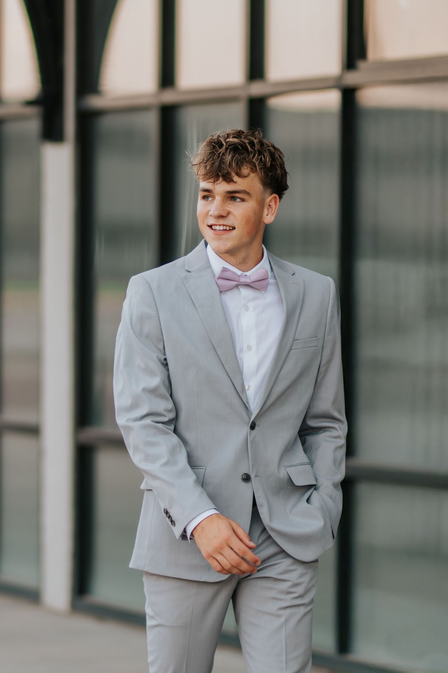 A person wearing a light gray suit and white shirt poses in front of a modern building exterior.