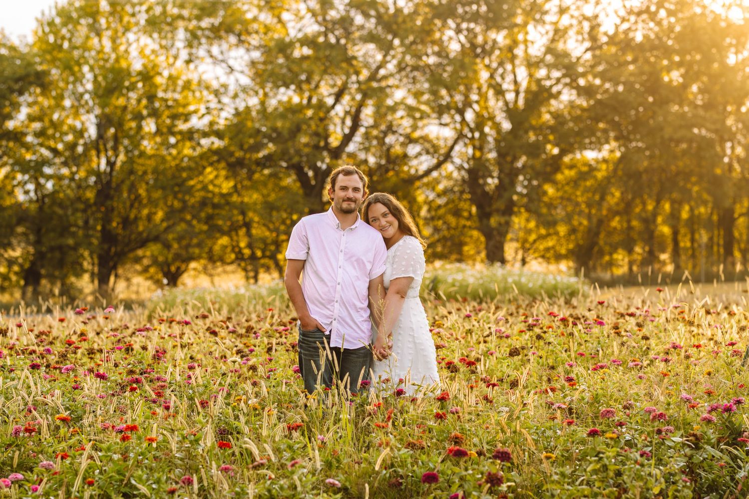 Couple standing together in a field of red flowers during golden hour.