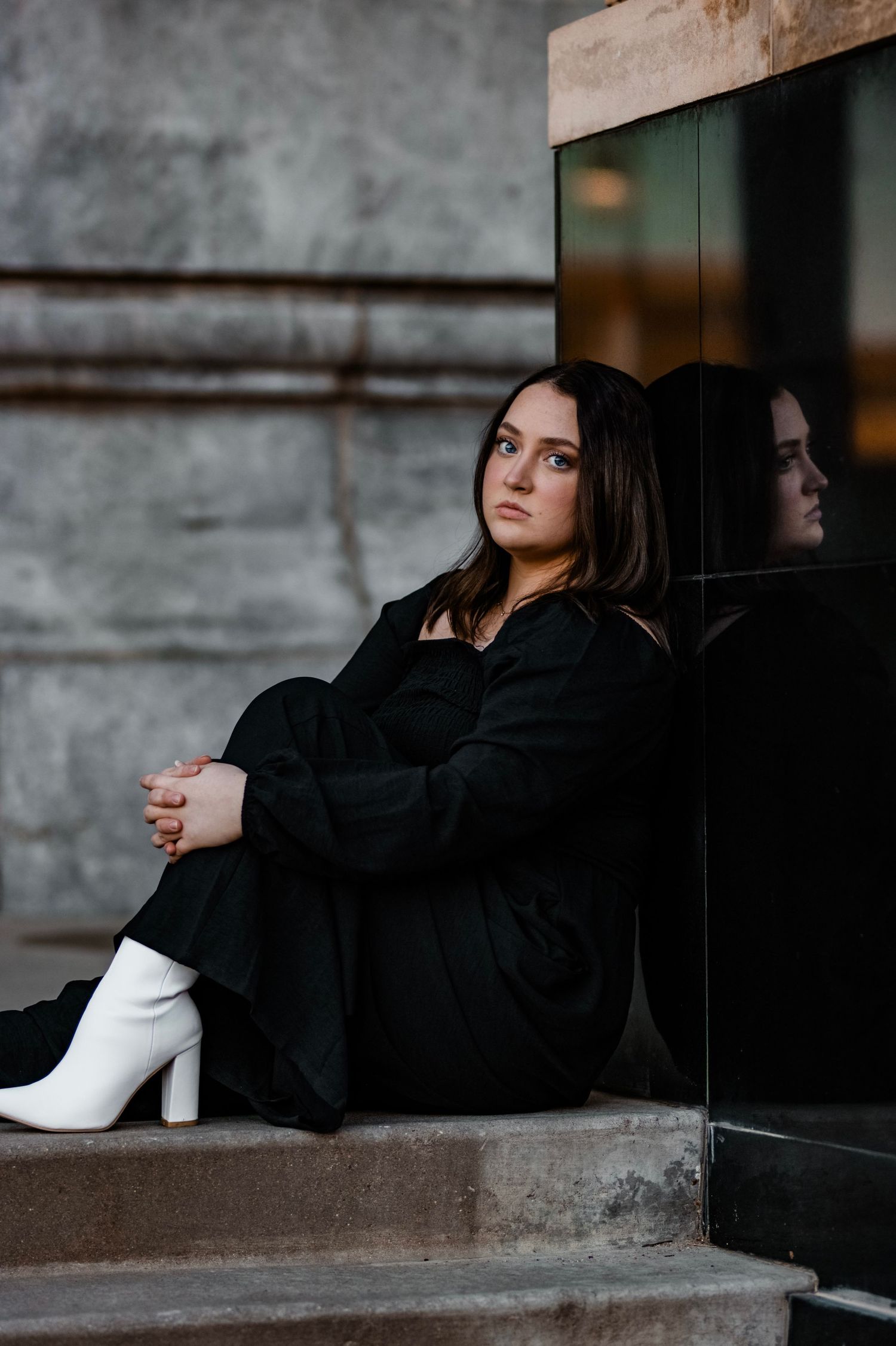 A woman in black sits on concrete steps wearing white boots in a moody portrait.