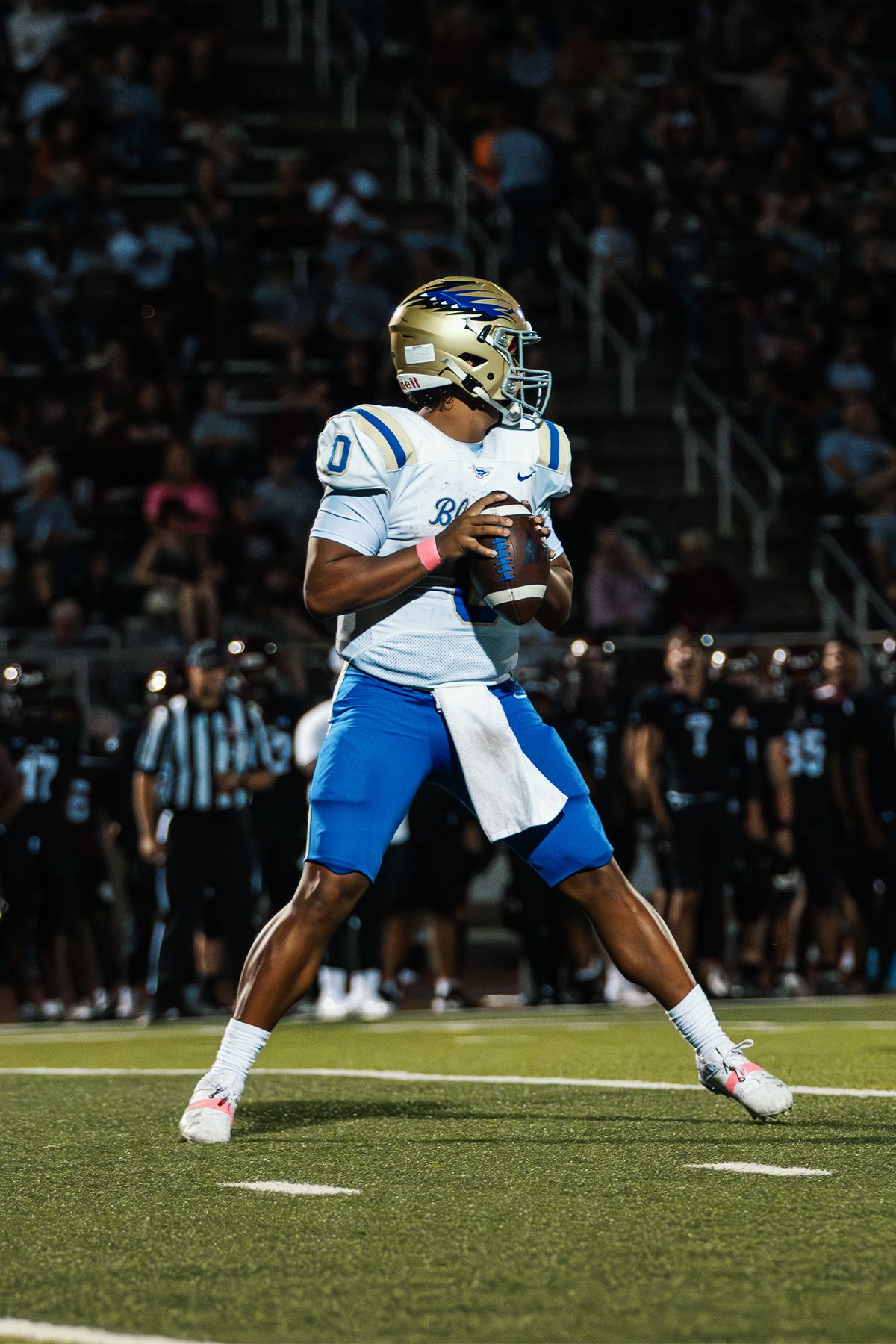 Football player in white and blue uniform prepares to throw pass during night game.