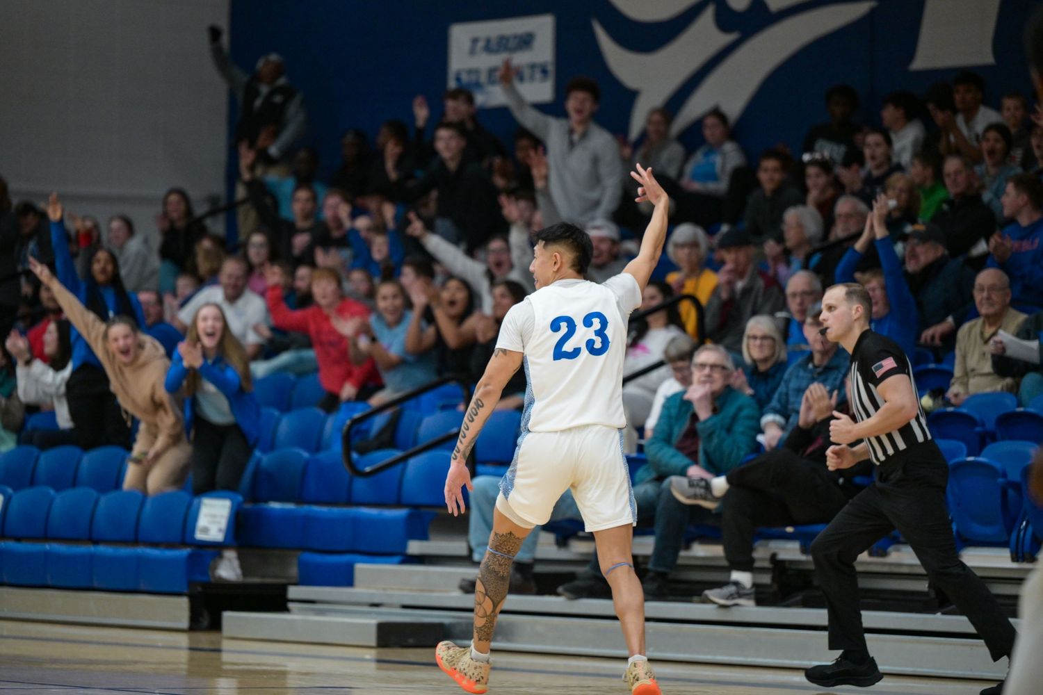 Basketball player in white jersey number 23 celebrates with arms raised during game.