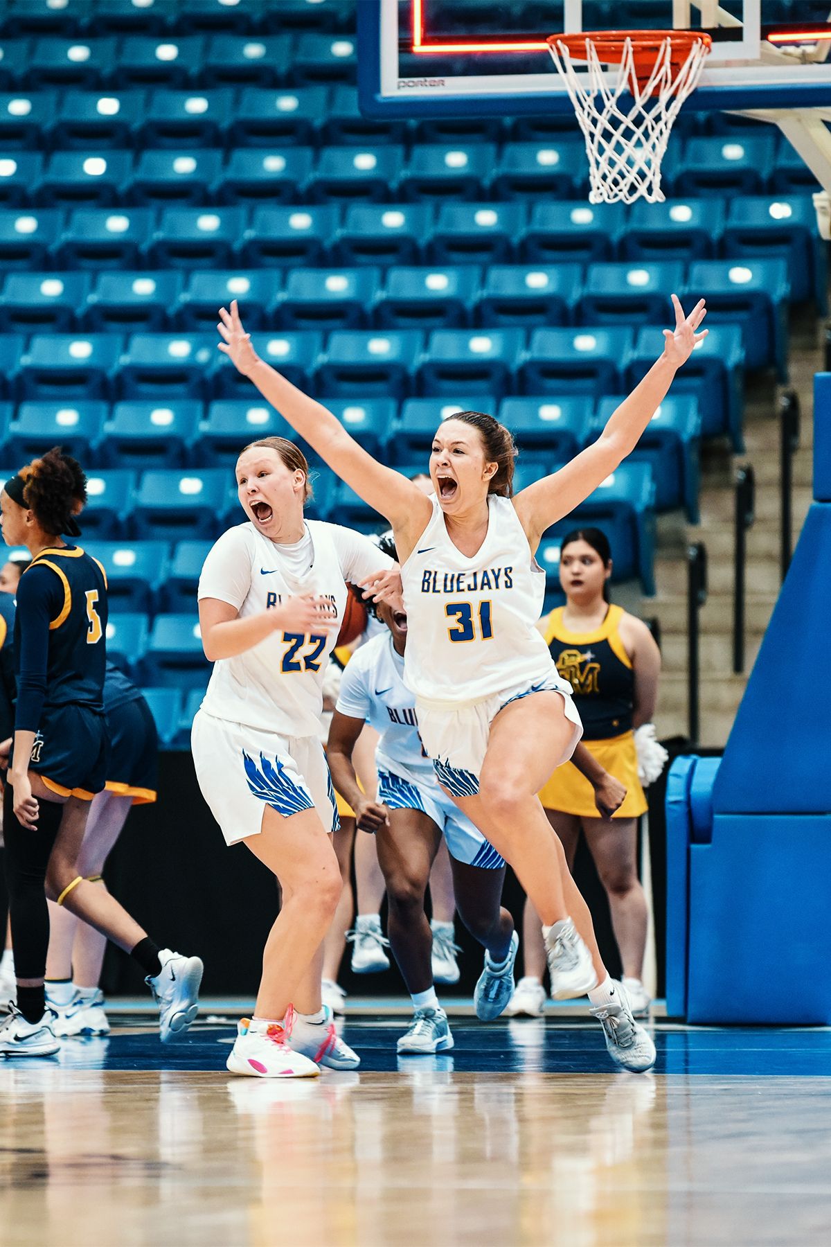 Basketball players celebrate enthusiastically during game in arena with blue seats.