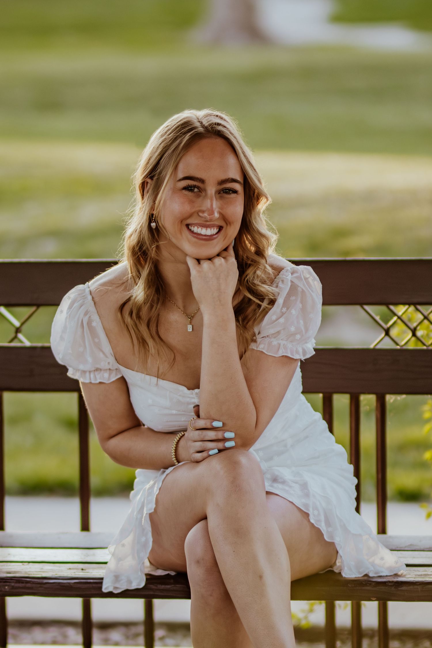 Person in white dress sits elegantly on wooden bench in park setting.