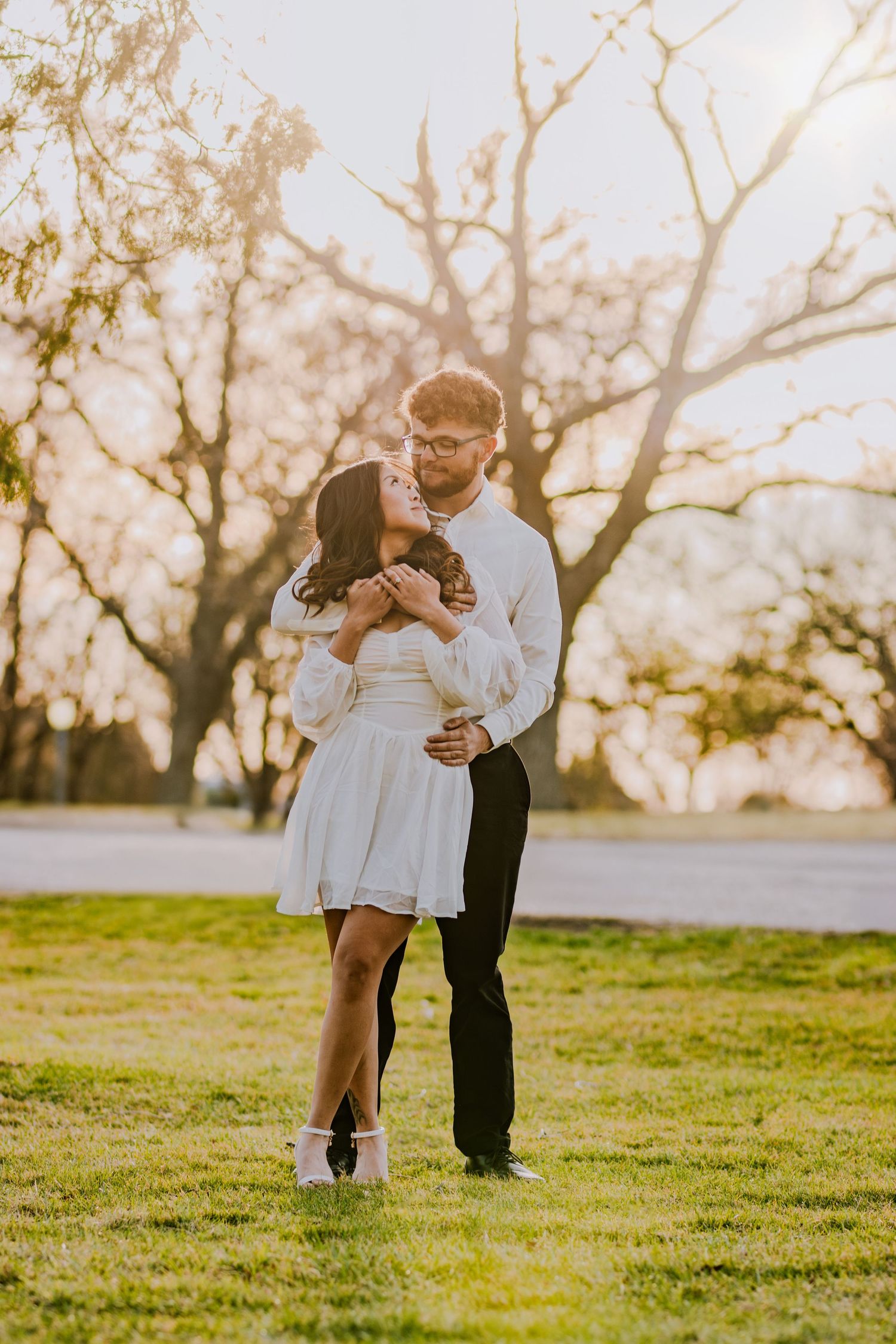 Romantic couple embracing on grassy field during golden hour sunset.