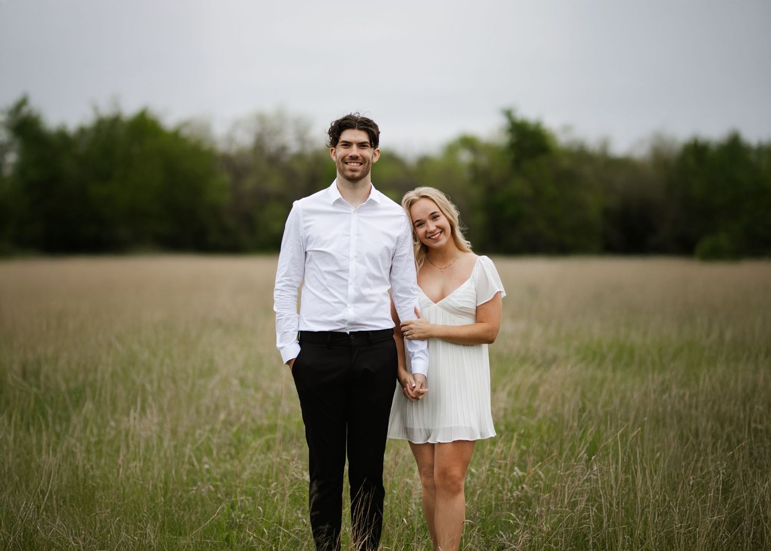 A happy couple stand together in a golden grassy field during a romantic outdoor photo session.
