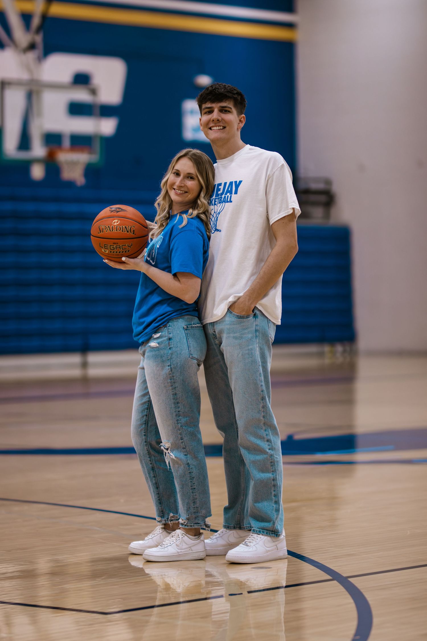 Playful couple posing with basketball on indoor court in casual athletic wear.