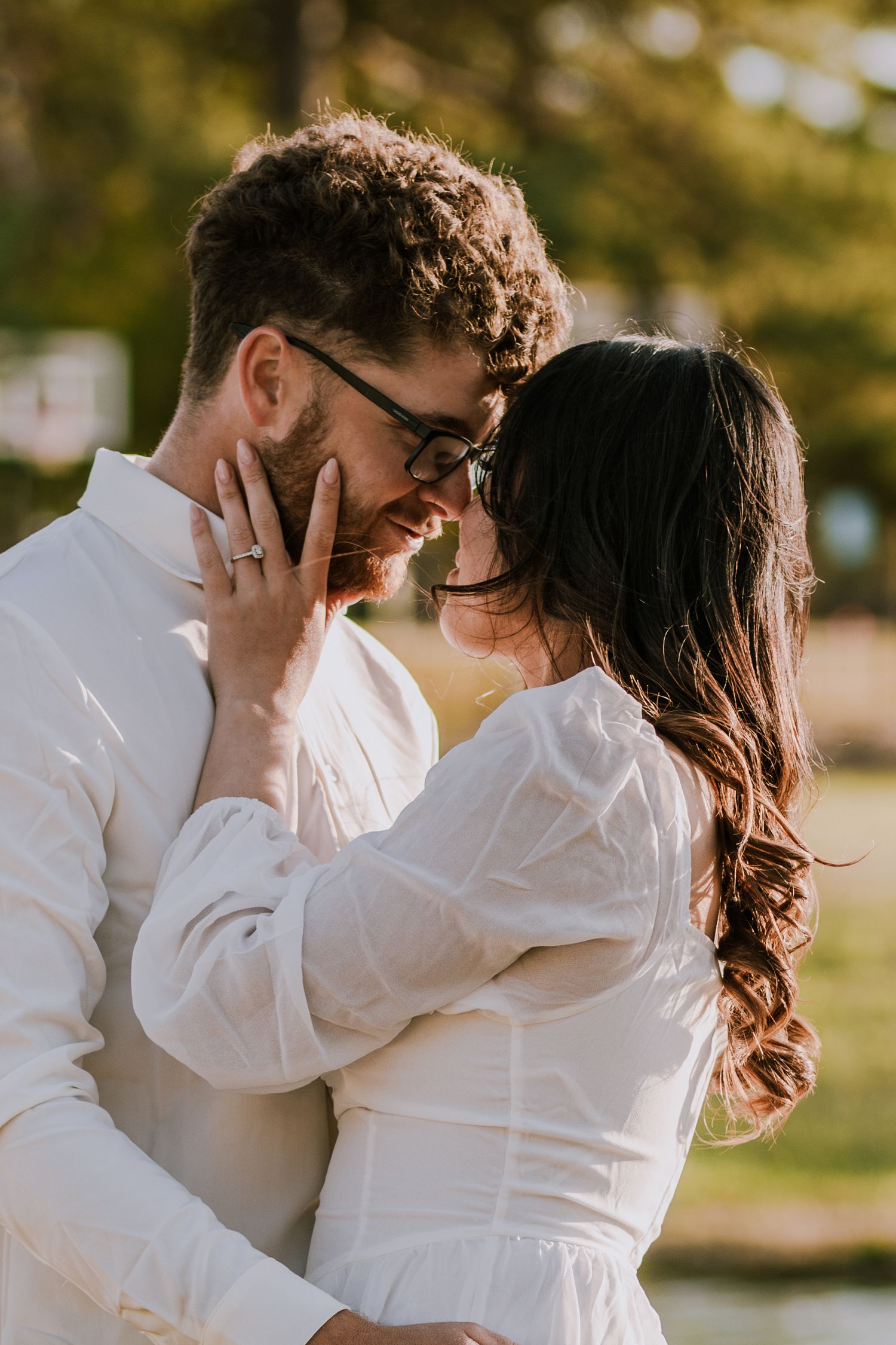 Romantic couple in white outfits sharing an intimate moment outdoors in warm sunlight.
