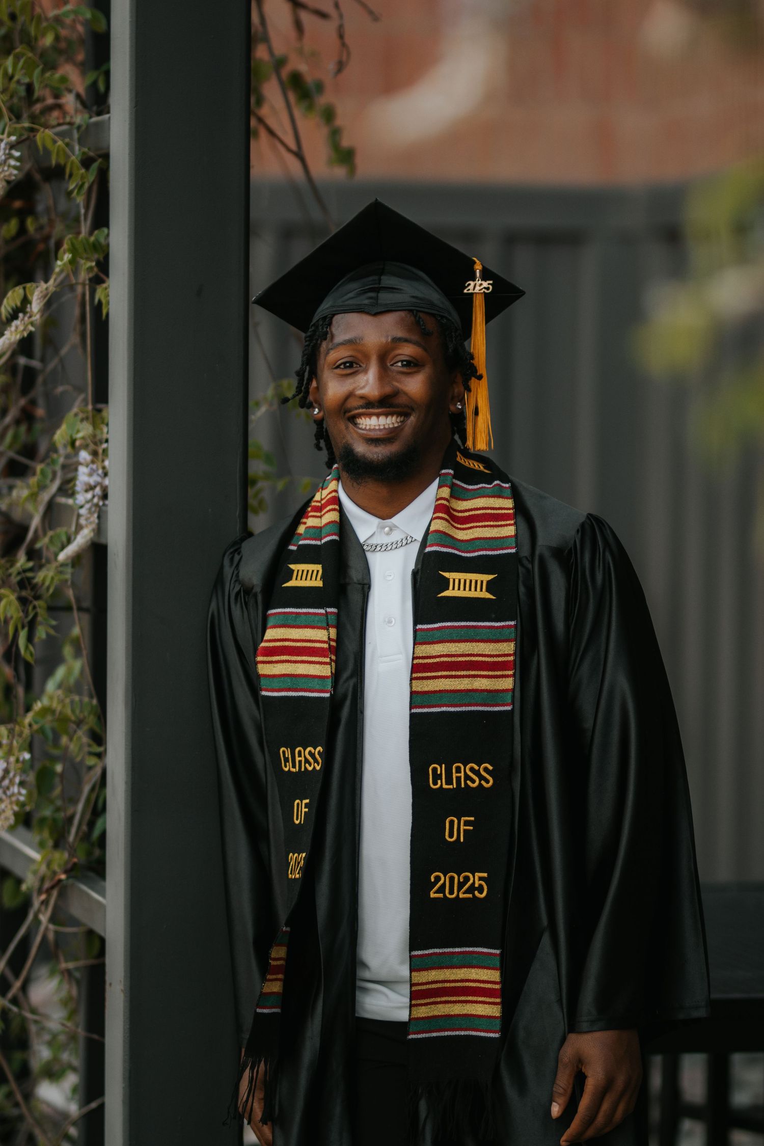 Graduate wearing traditional black graduation gown and decorative kente stole celebrating Class of 2025.