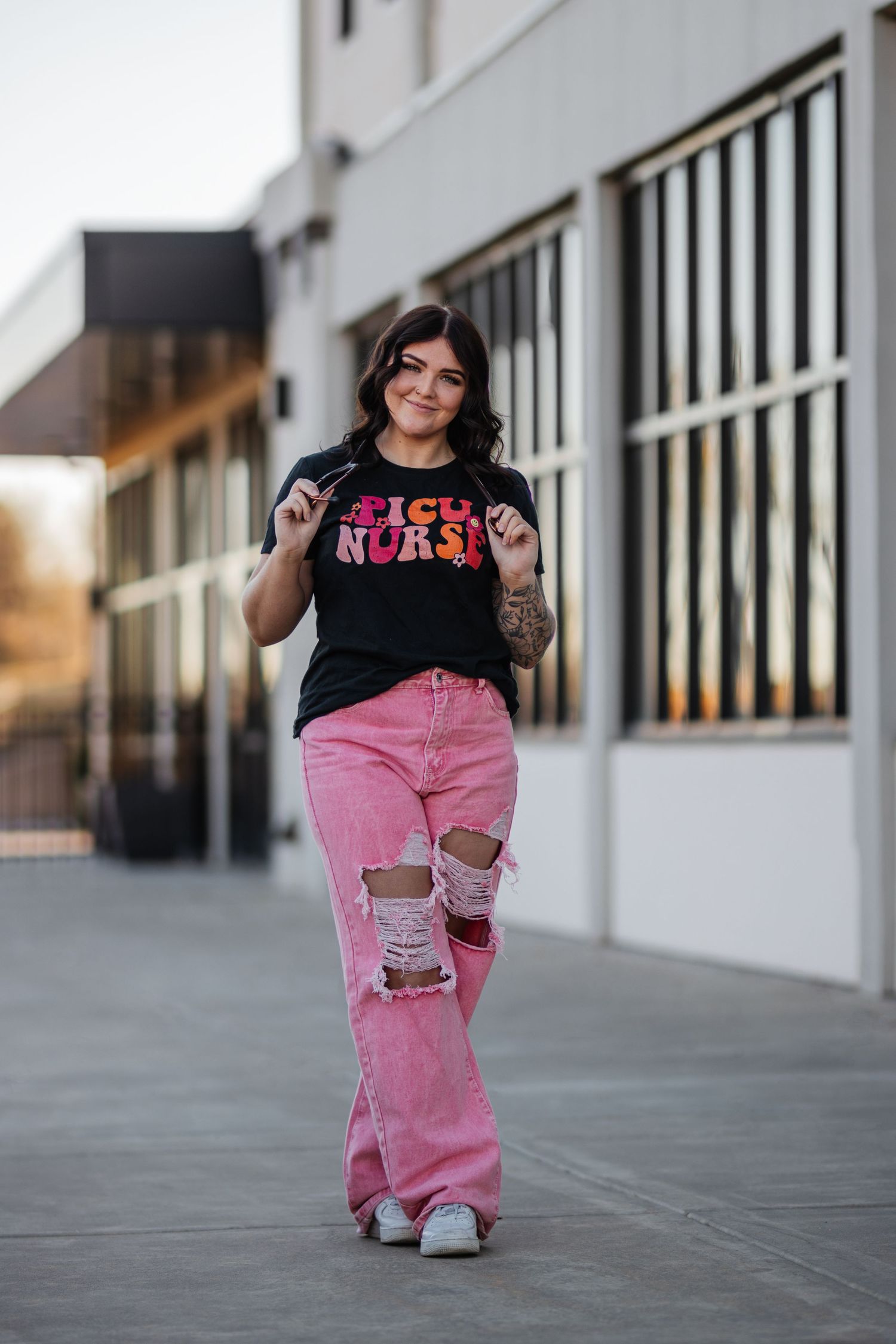 Person in black t-shirt and distressed pink jeans posing against urban building wall.
