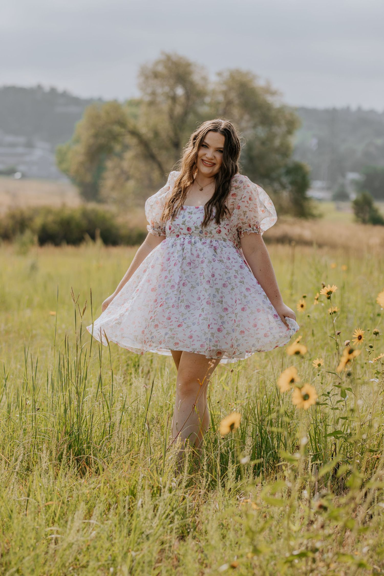 A person in a floral dress twirls playfully in a sunlit meadow with yellow wildflowers and tall grass.
