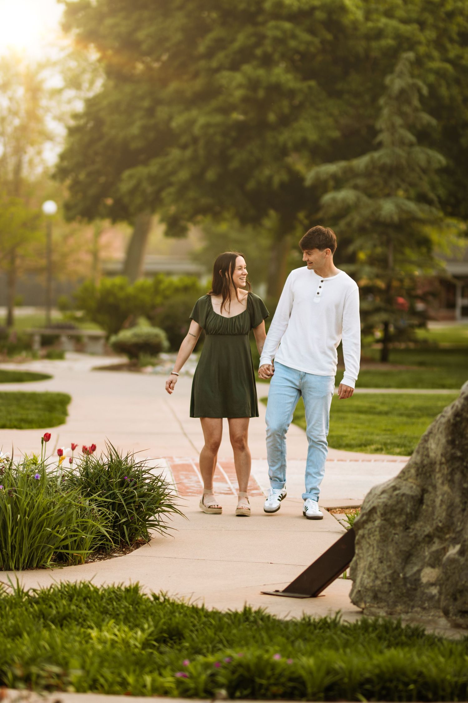 A couple walking together on a garden pathway during golden hour sunset while holding beverages.