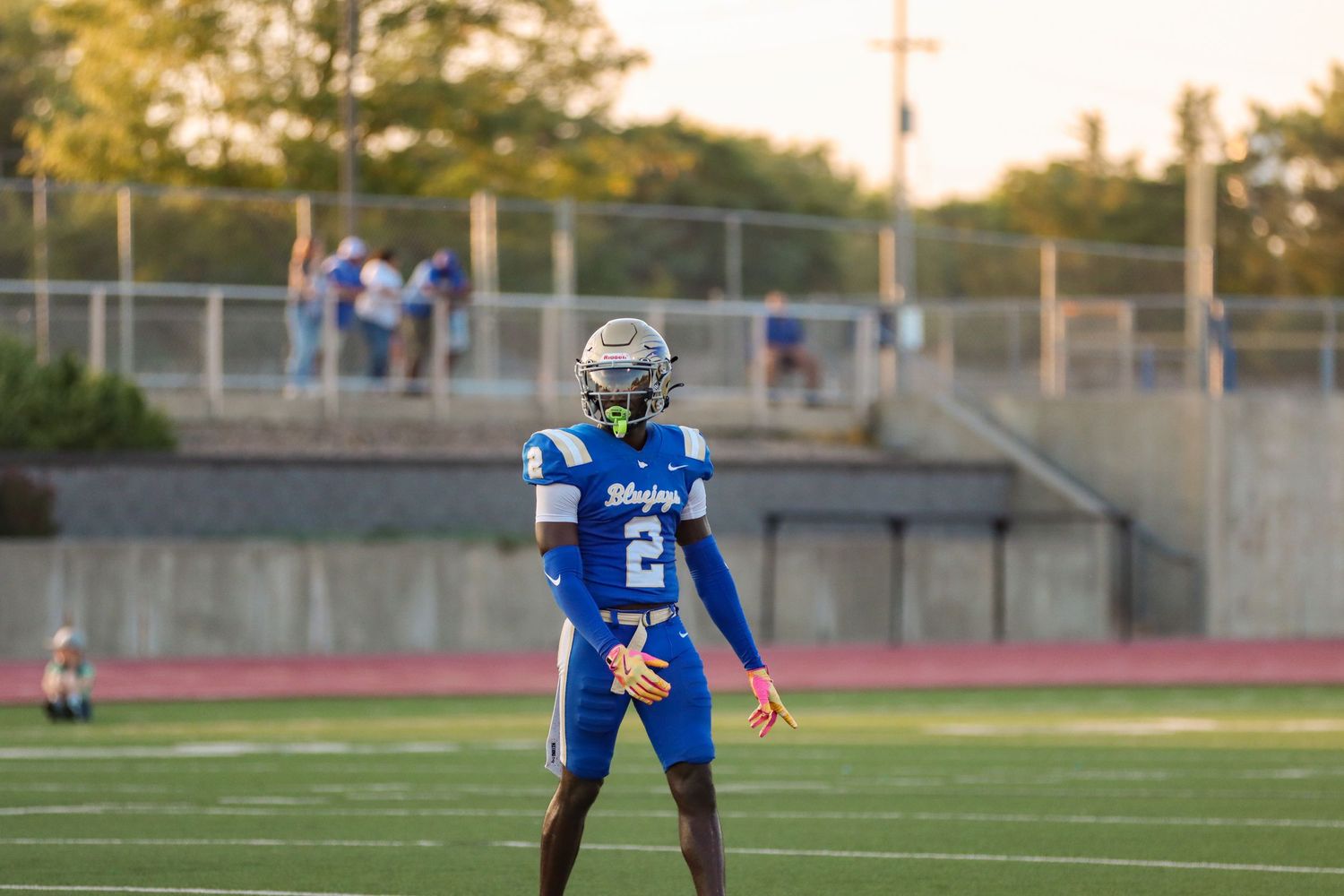 Football player in blue jersey stands ready on field during evening game.