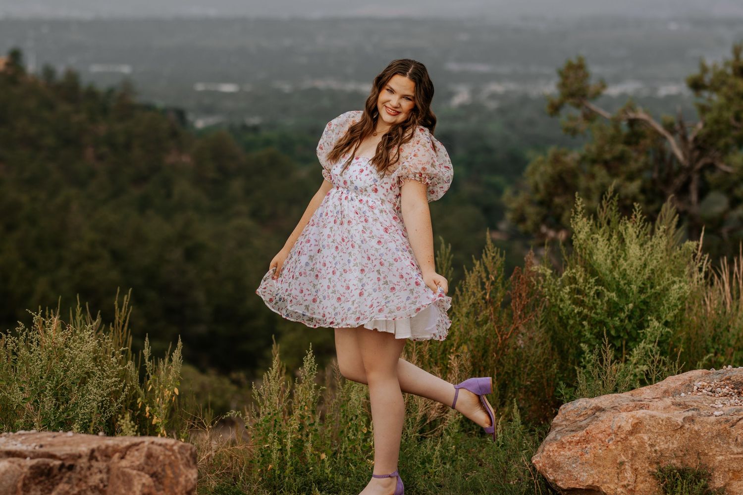 A floral dress and pink sneakers complement a scenic mountain overlook at sunset.