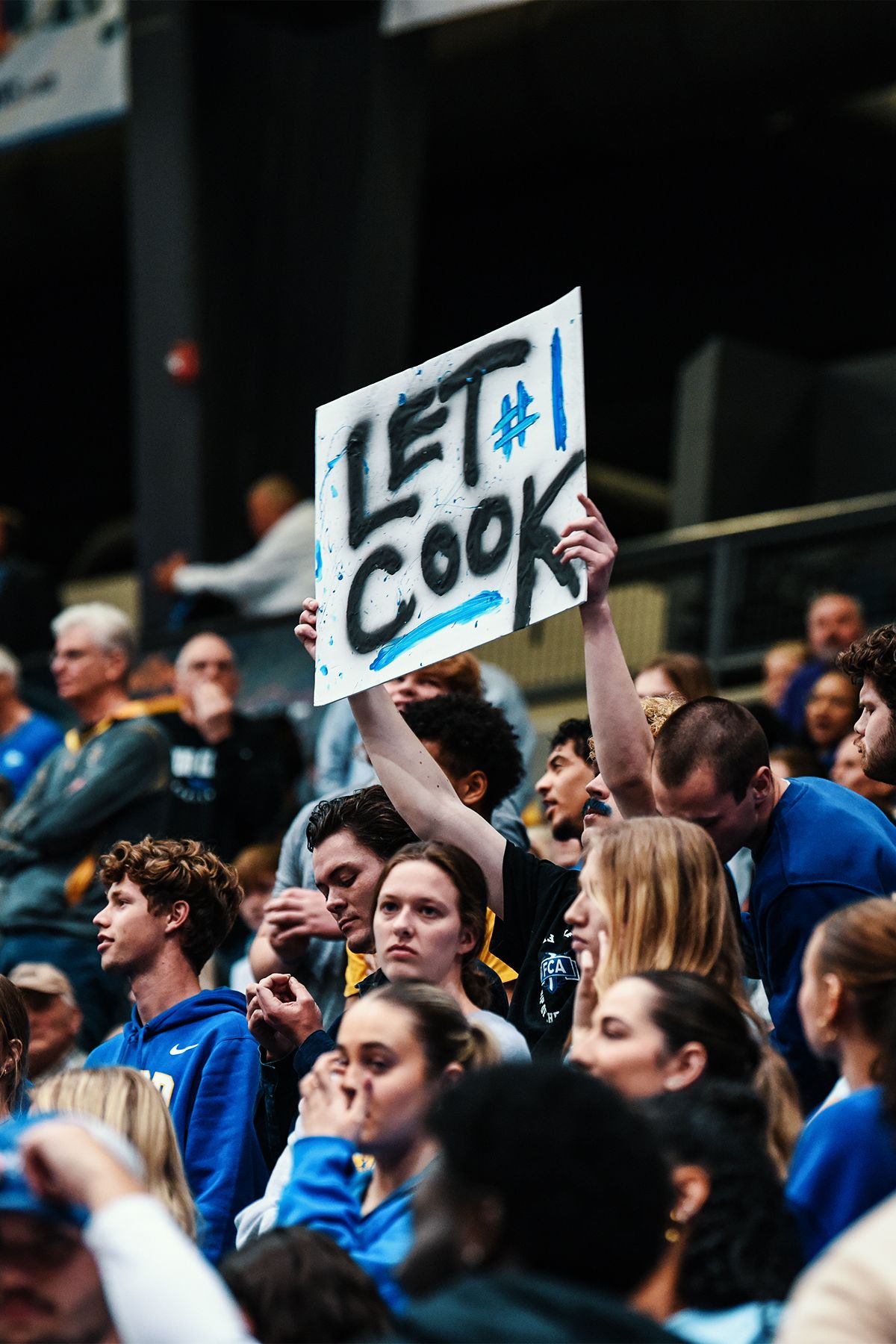 Fans in crowd hold up 'Let's Go' sign during sporting event.