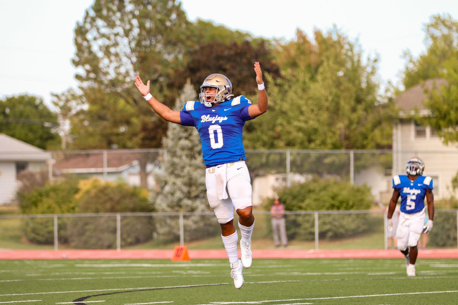 Football player celebrates with arms raised wearing blue jersey number zero.
