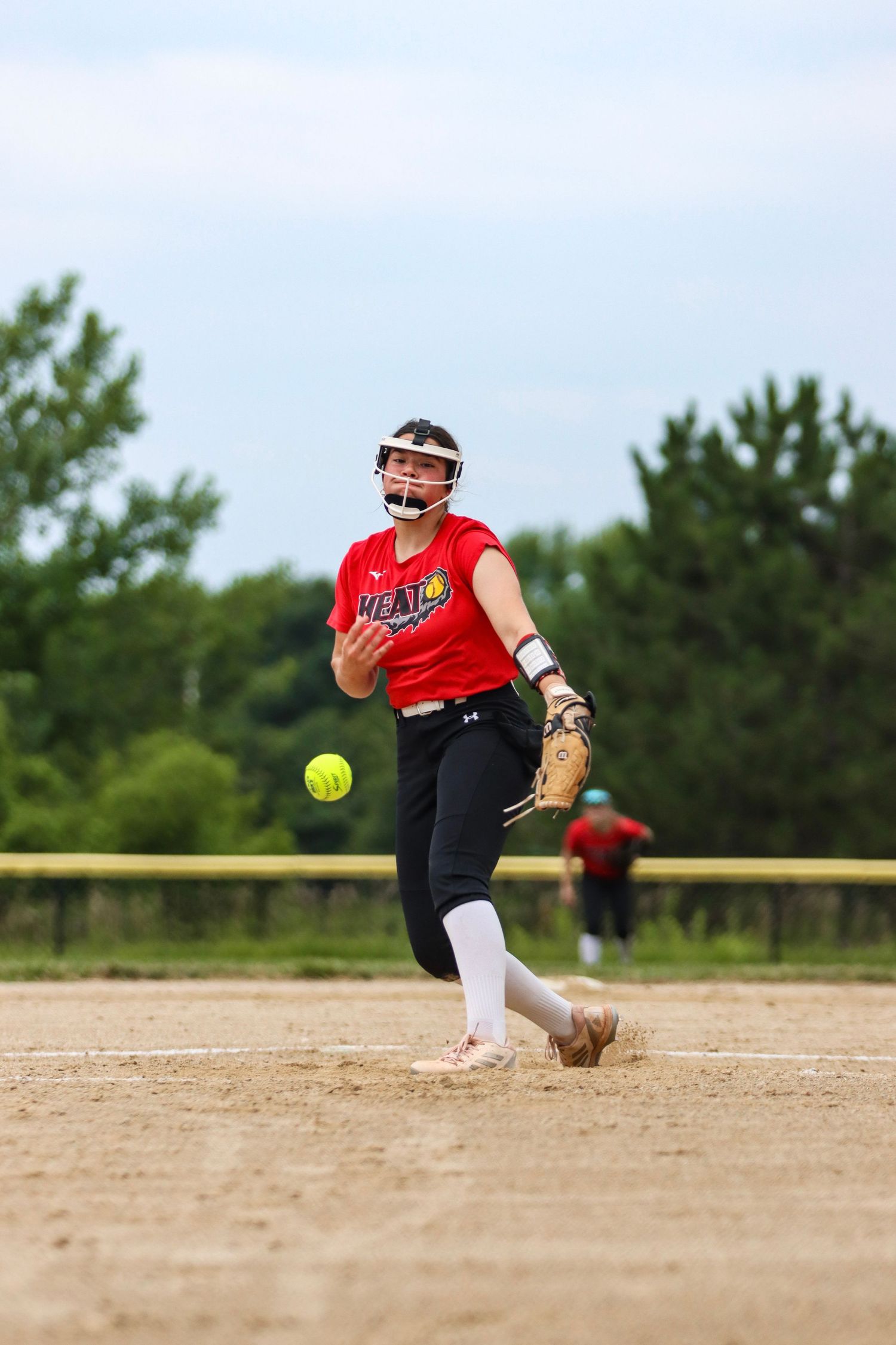 Softball pitcher in red uniform mid-delivery motion on dirt mound.