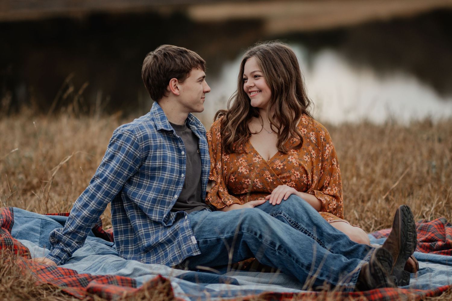 A couple shares intimate moments on a picnic blanket in a golden autumn field at sunset.