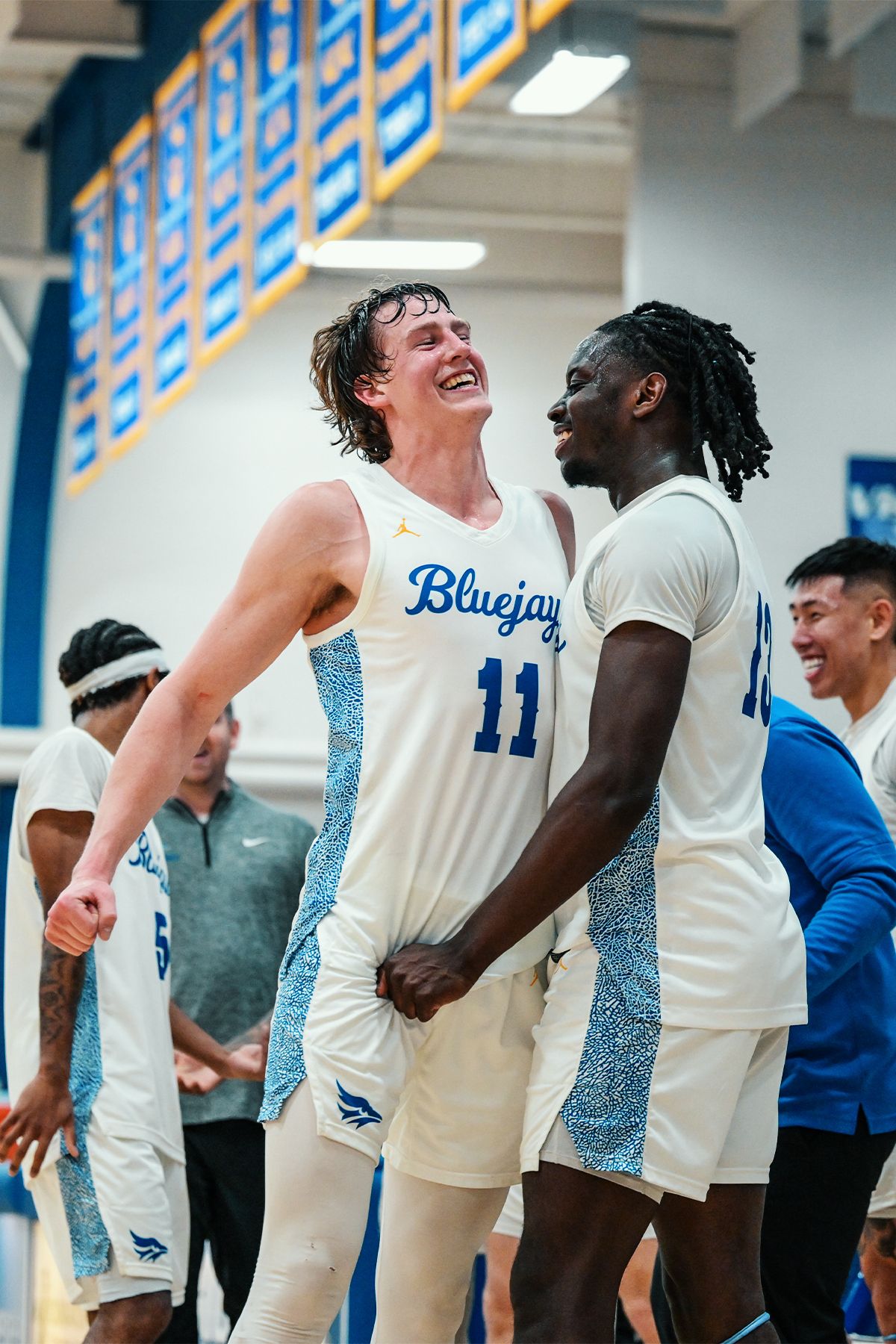 Basketball teammates in white Bluejays jerseys share a lighthearted moment during game.
