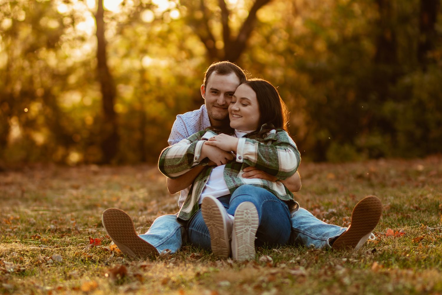 A couple sitting together on grass during golden hour surrounded by autumn trees.