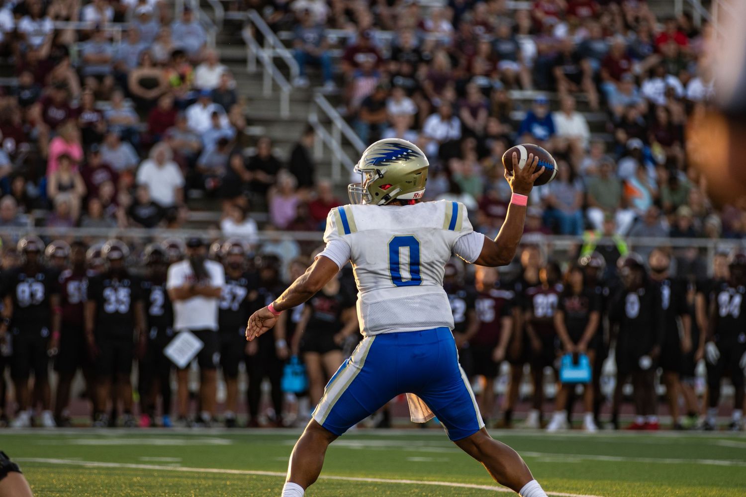 Football player in blue uniform jumps to catch ball during night game.
