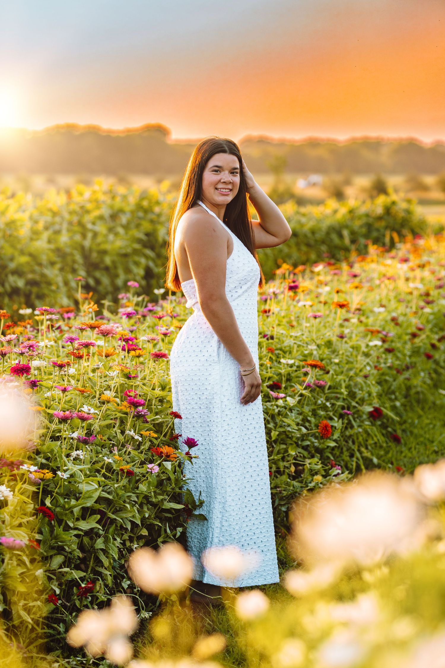 A sunset photoshoot in a vibrant flower field with red zinnias and wildflowers during golden hour.