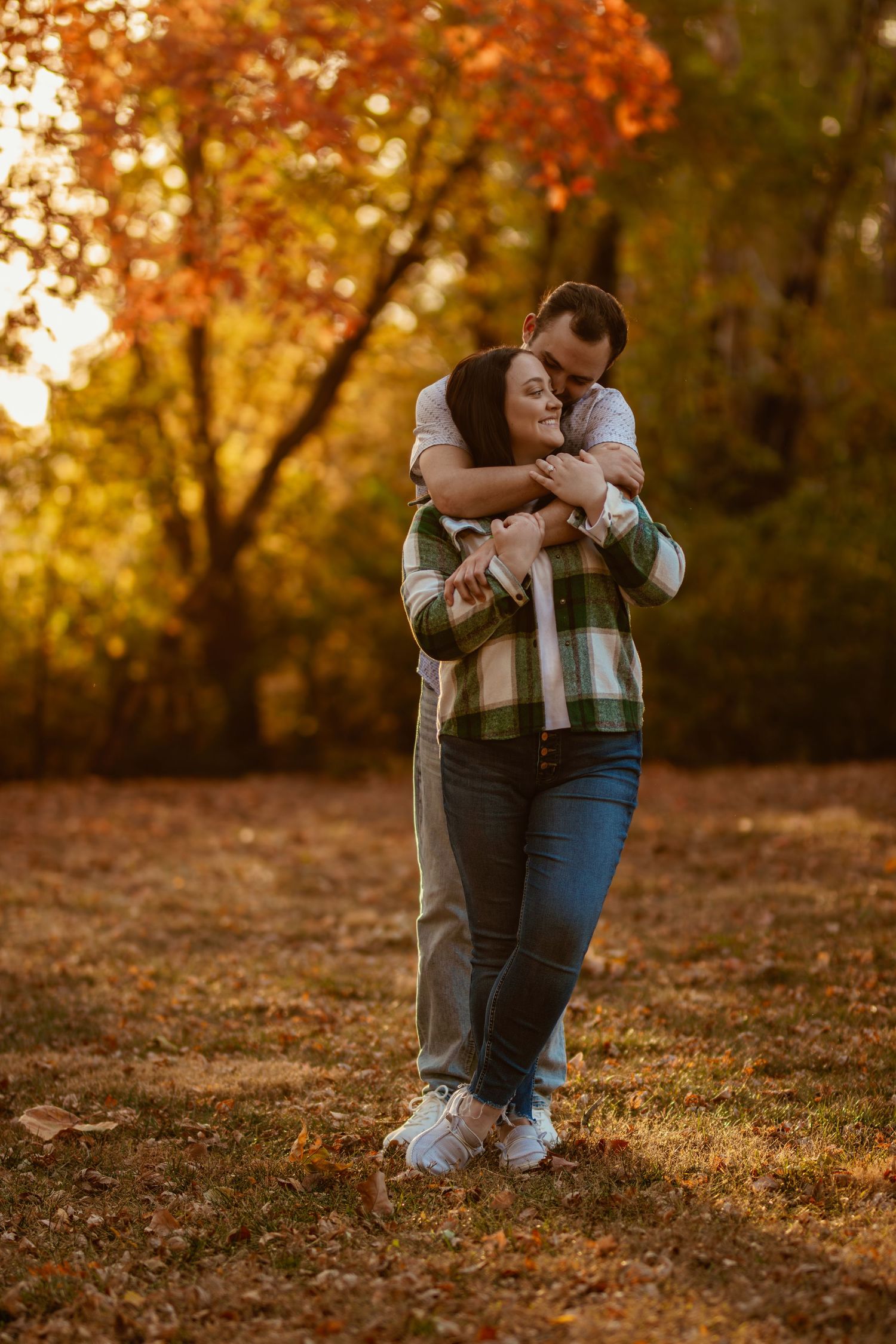 A couple sharing an intimate embrace while standing on fallen autumn leaves in a park.