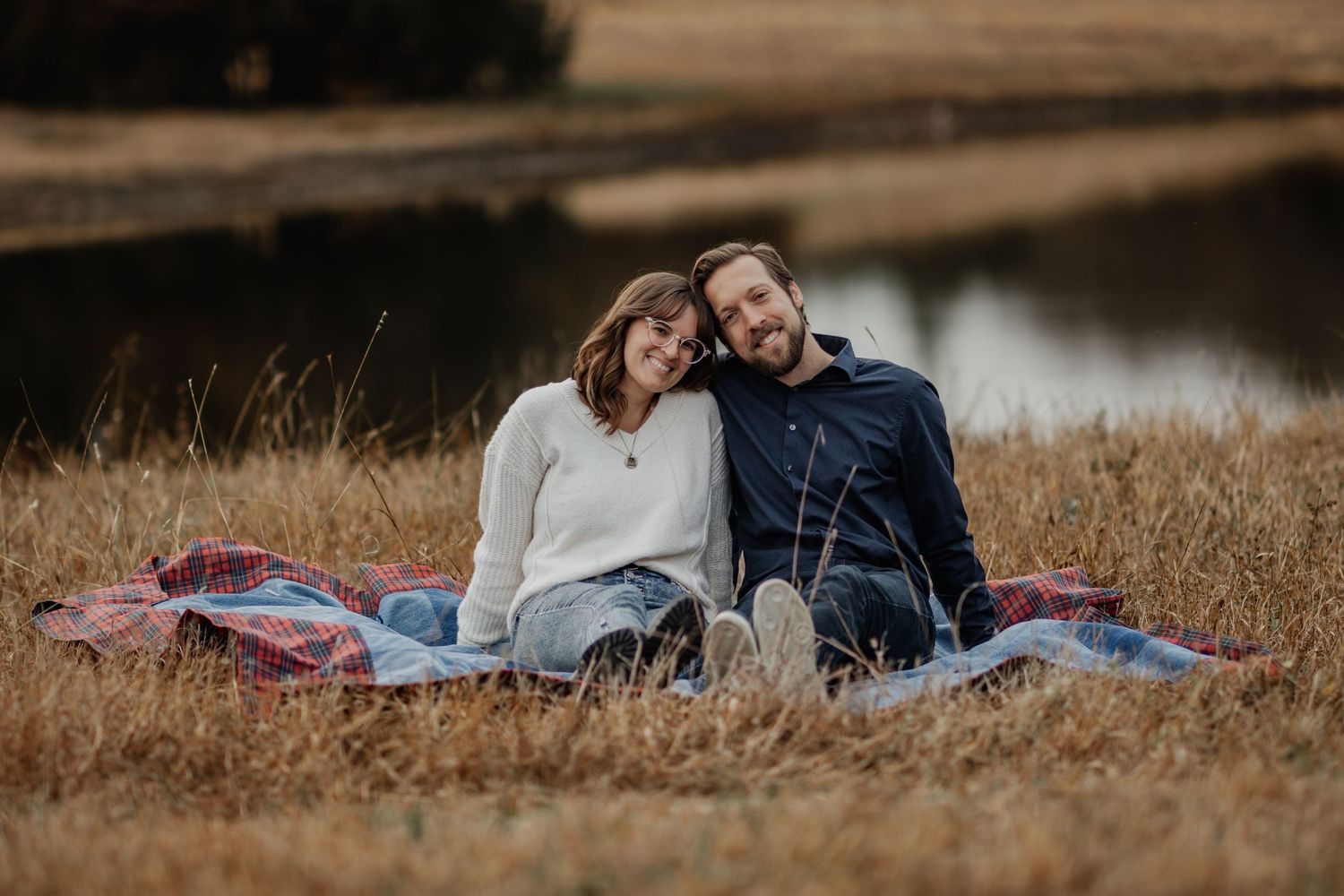 A couple lies together in a golden grassy field during a romantic outdoor photo session at sunset.